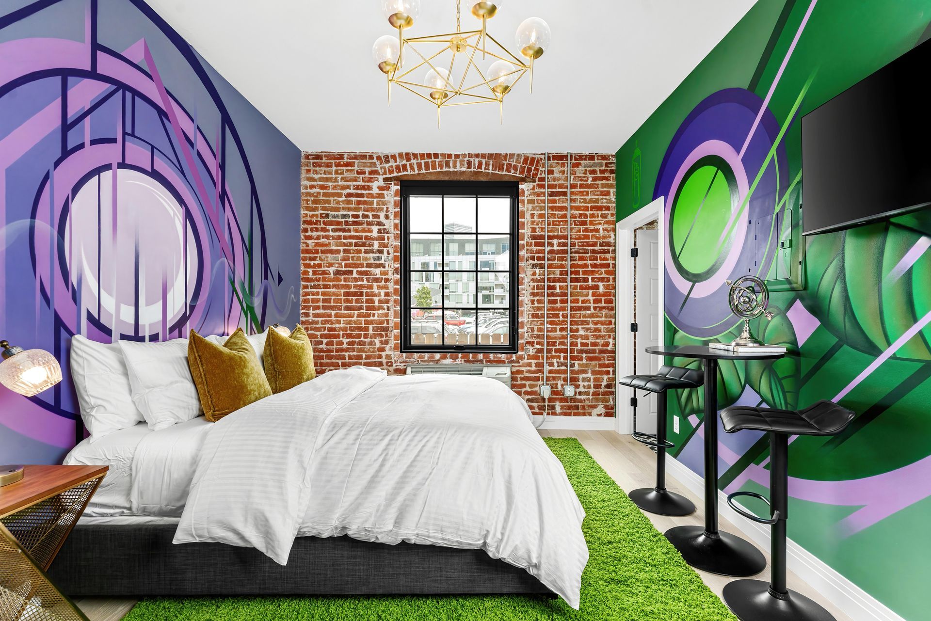 Modern bedroom with colorful graffiti mural walls, white bed, brick accent wall, and green rug