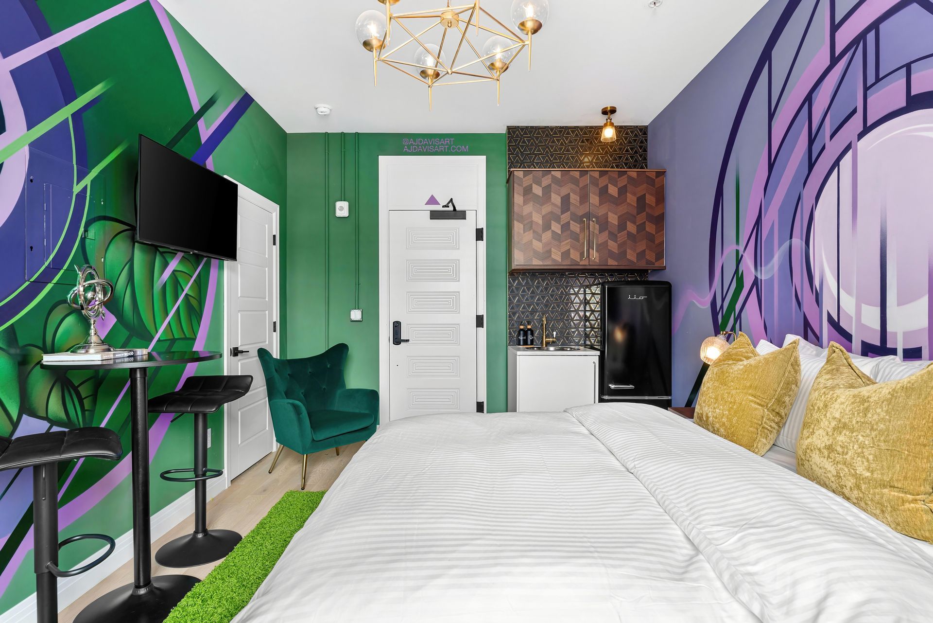 Colorful modern bedroom with a bed, TV, green accents, and purple graffiti-style wall art
