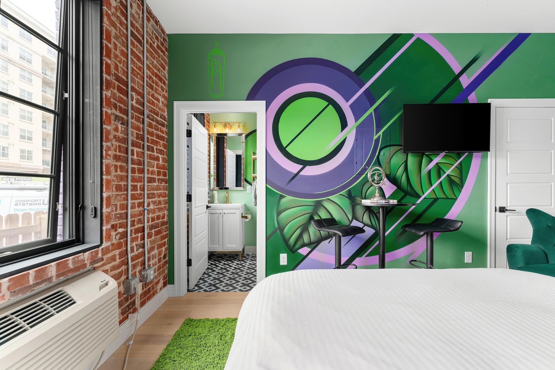 Modern bedroom with graffiti mural wall, white bed, brick window wall, and green rug