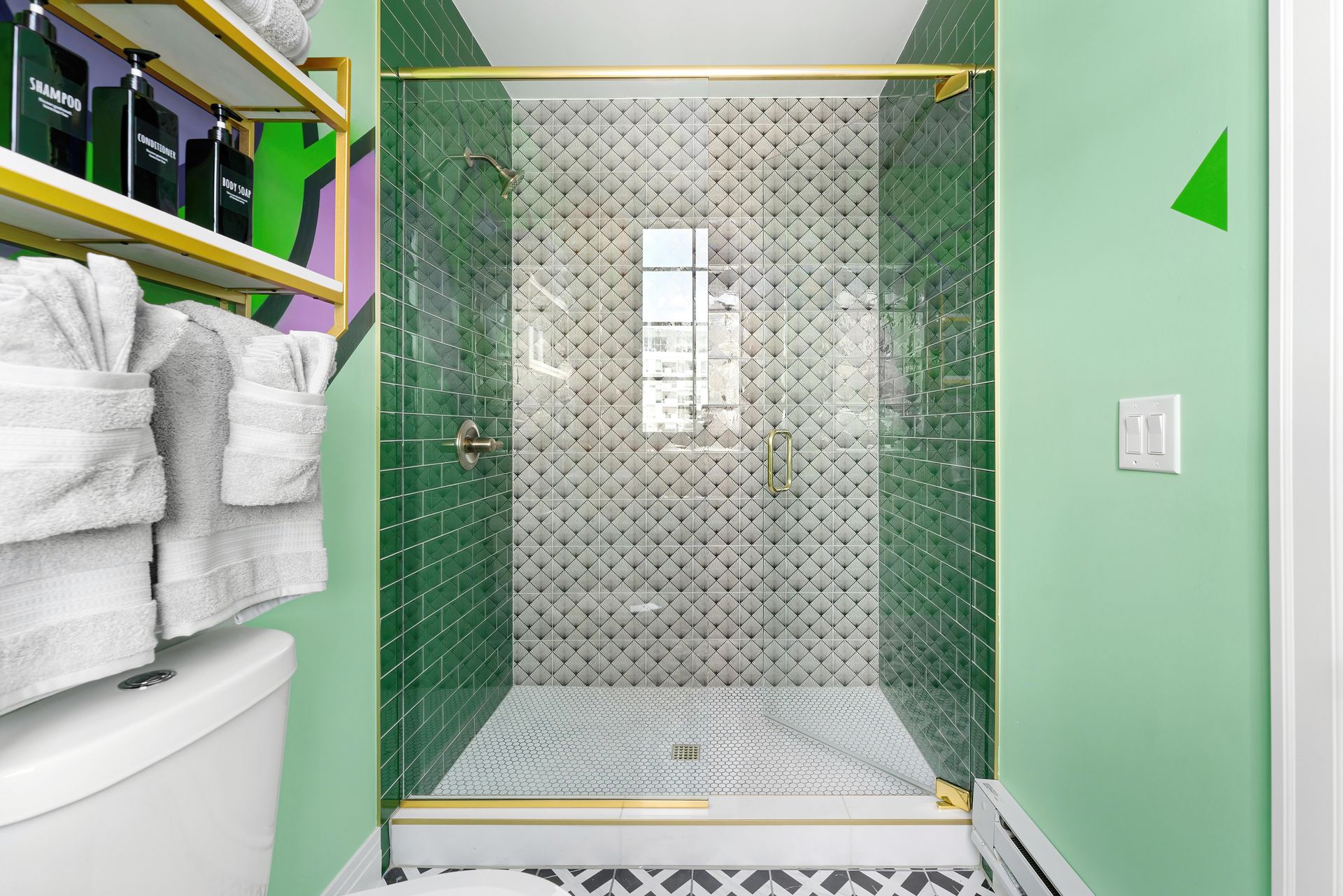 Green-tiled shower with glass door, towel shelf, and mint walls in a small bathroom