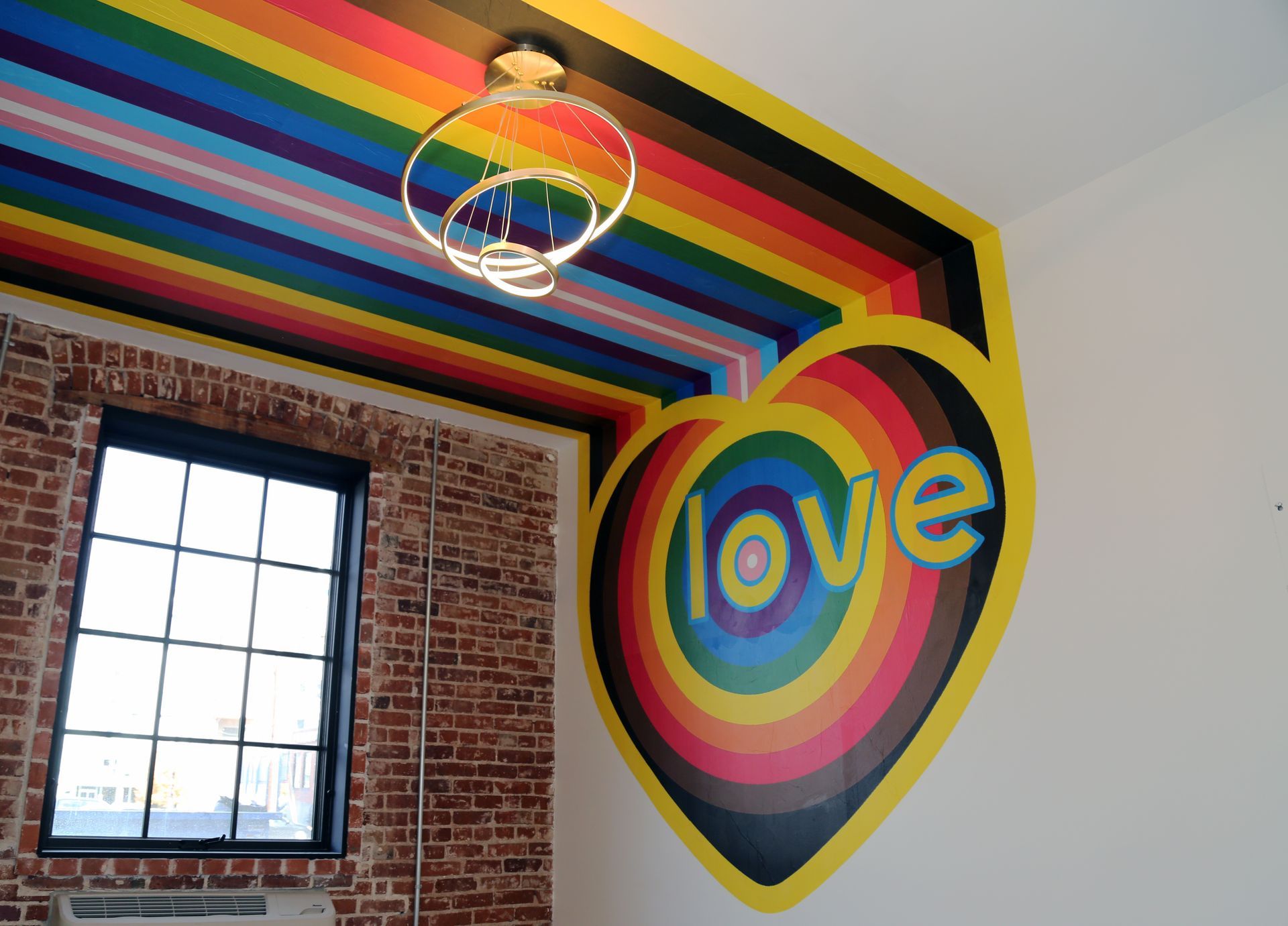 Rainbow-painted room with a brick wall, window, and a large colorful heart reading “love”