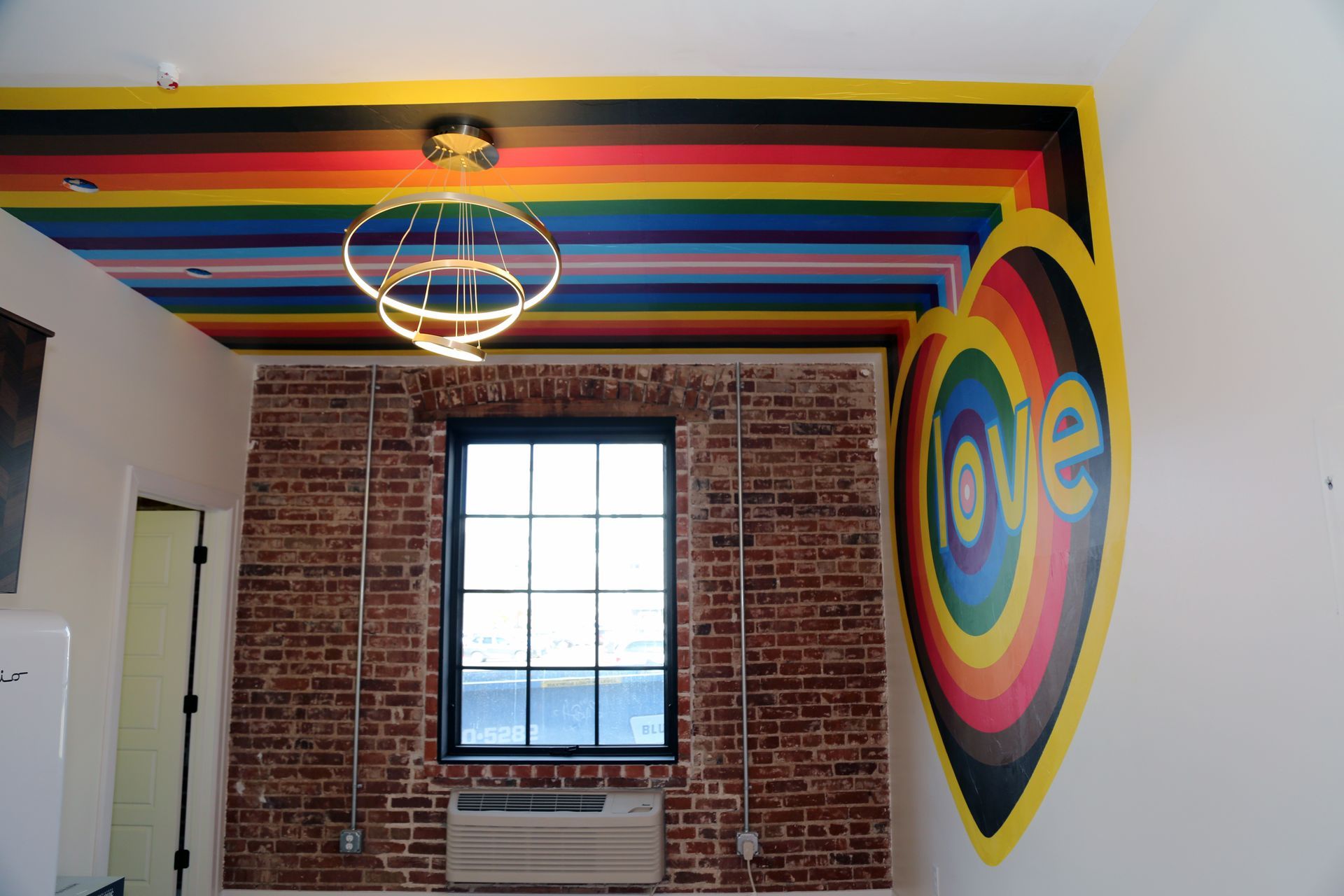 Rainbow ceiling mural and heart-shaped “love” wall art in a bright room with exposed brick wall