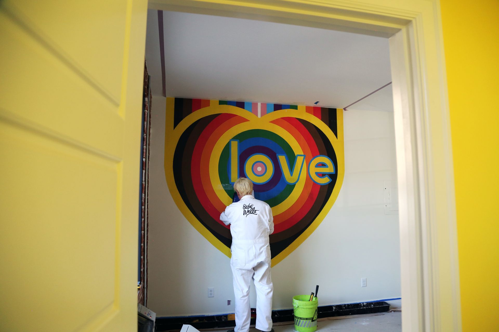 Person painting a colorful rainbow heart mural with the word “love” on a wall.