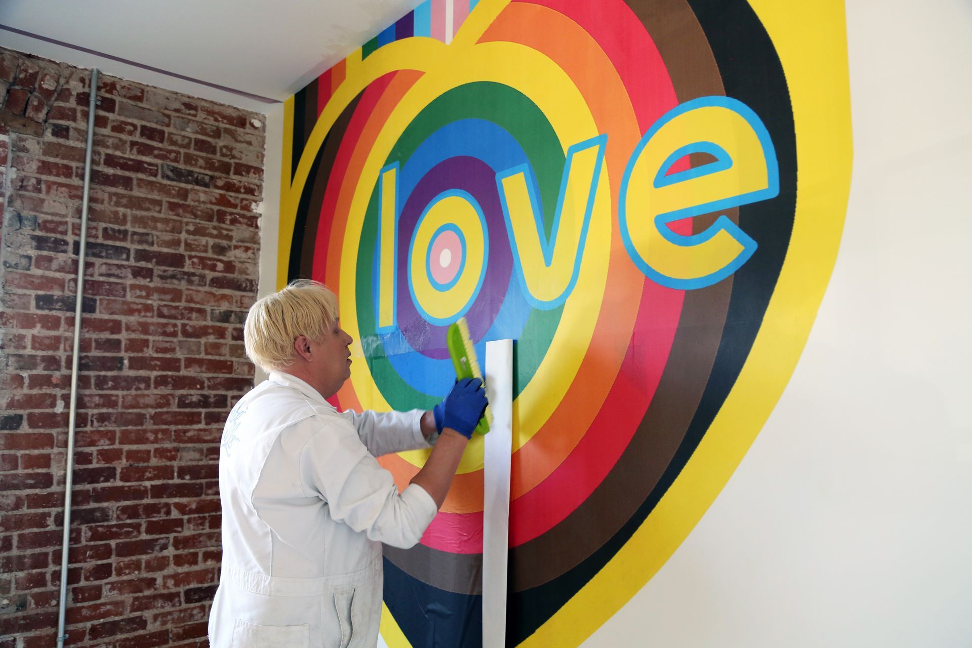 Person painting a colorful rainbow heart mural with the word “love” on a wall