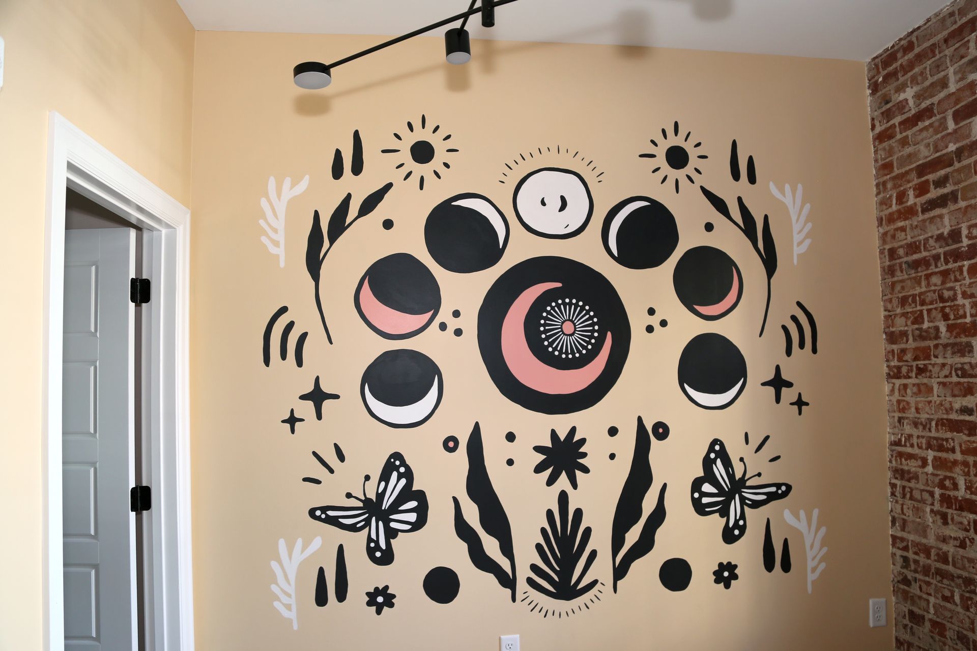 Mural with black, pink, and white celestial and botanical symbols on a tan wall in a room