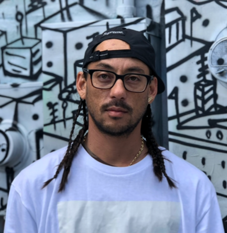 Man in black cap and glasses in front of a black-and-white mural wall.