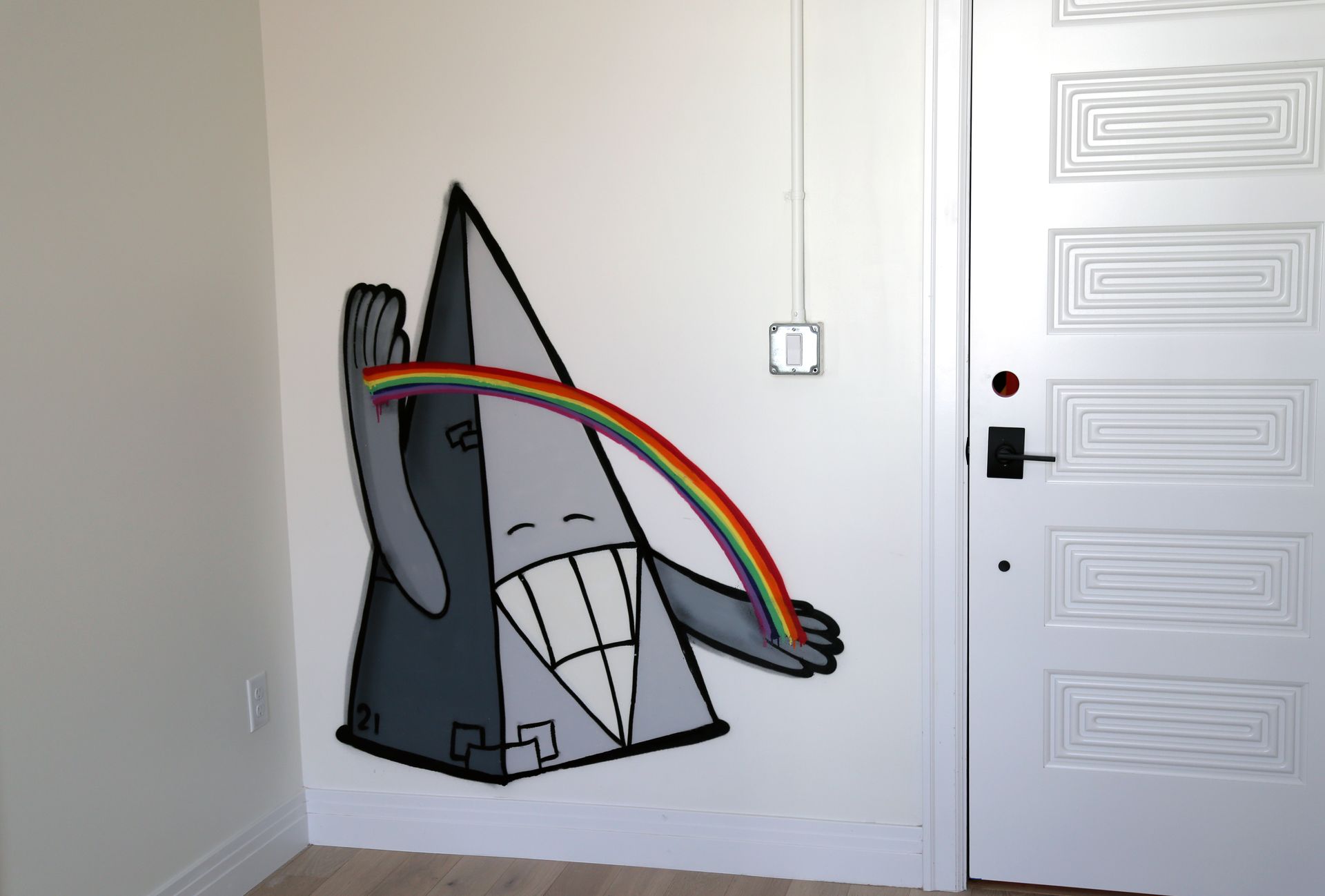 Cartoon gray shark mural with a rainbow arcing across it on a white interior wall.