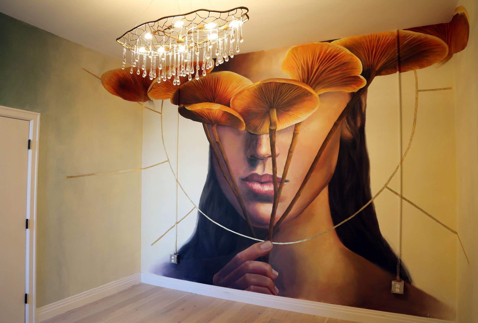 Large mural of a woman's face with orange mushrooms and hanging crystal chandelier in a modern room