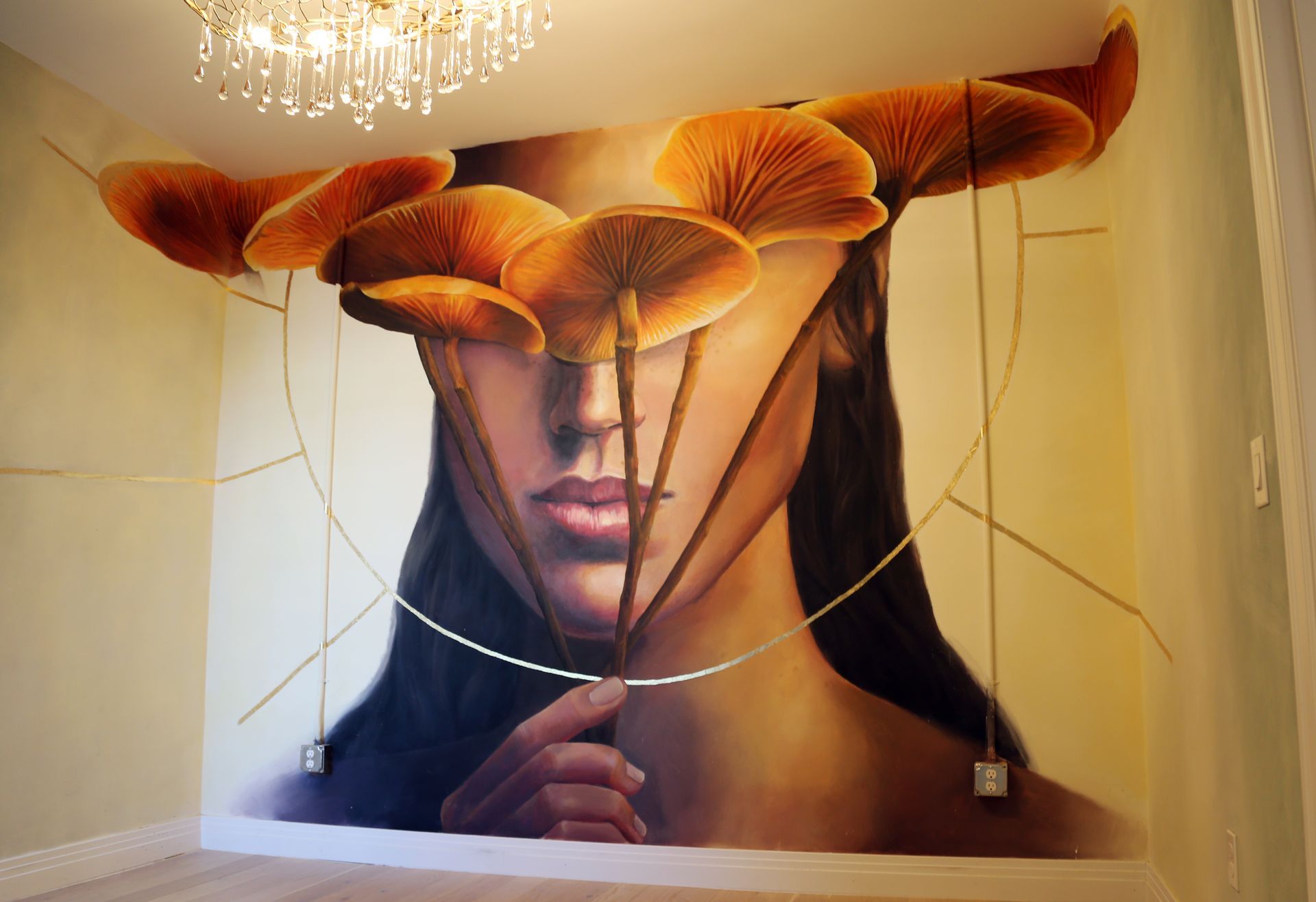 Mural of a woman with mushrooms over her eyes beneath a chandelier on a wall