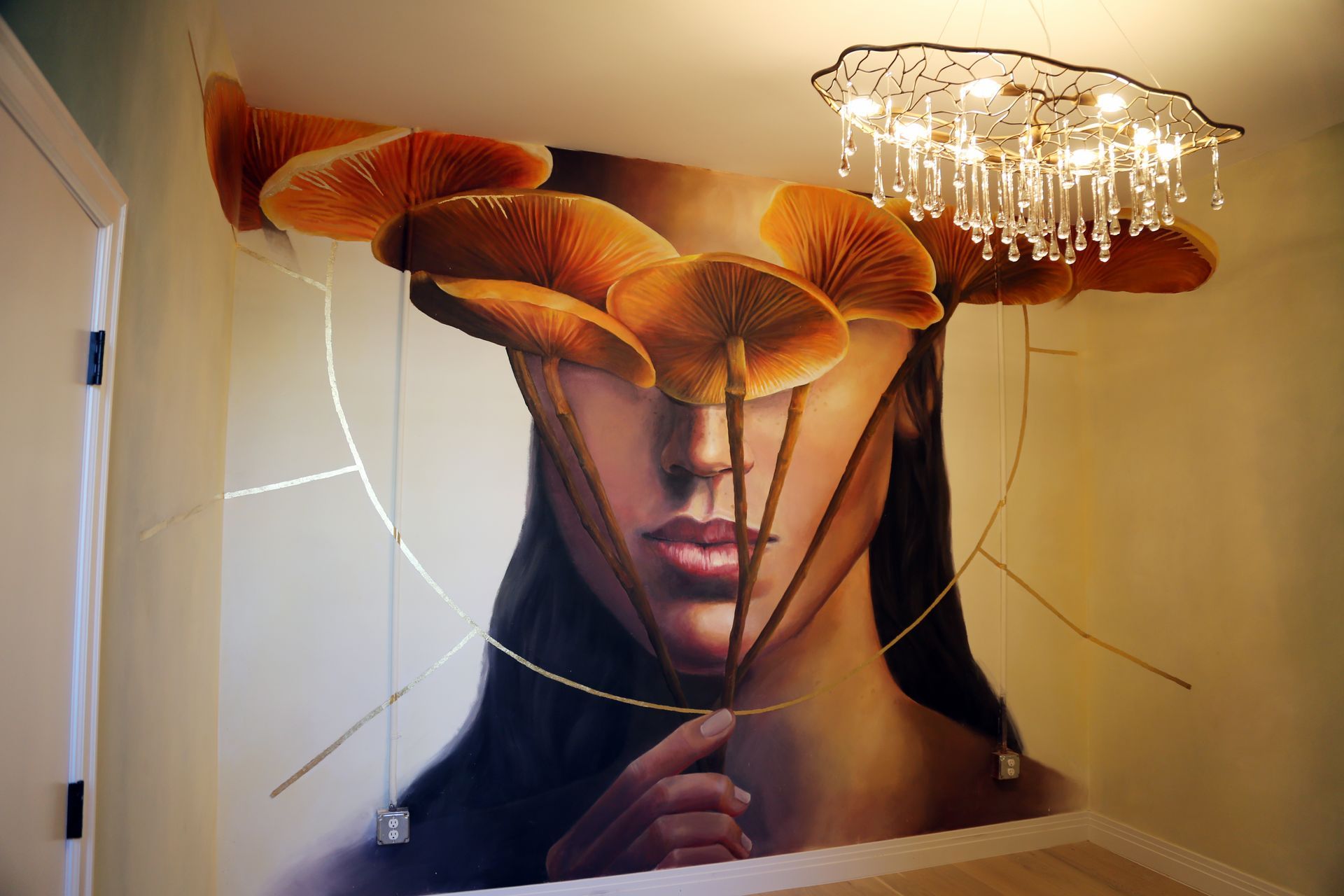 Surreal portrait mural of a woman with orange mushrooms covering her eyes and a chandelier above her head
