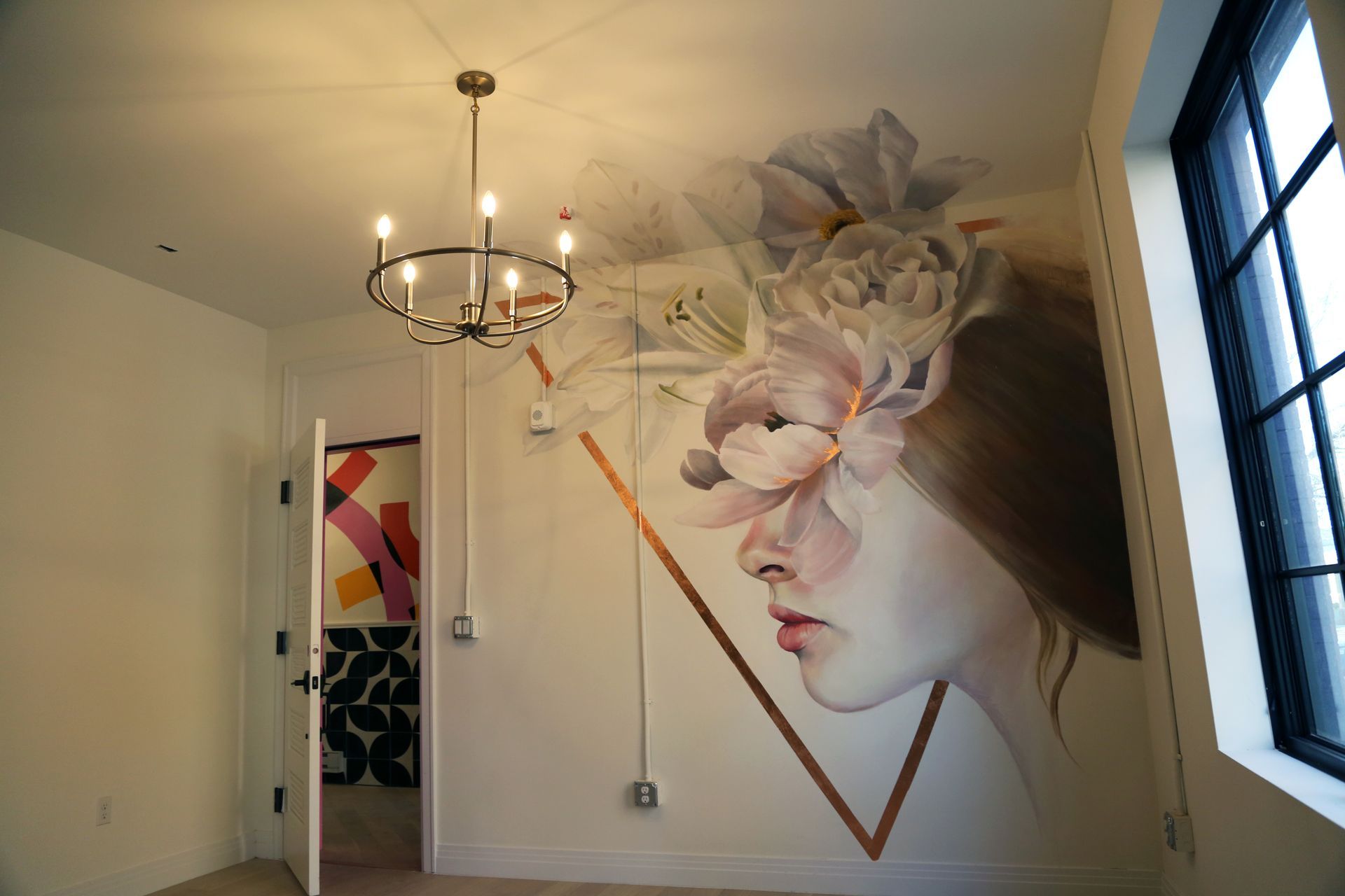 Interior wall mural of a woman's profile with a large flower, beside a chandelier and open doorway.