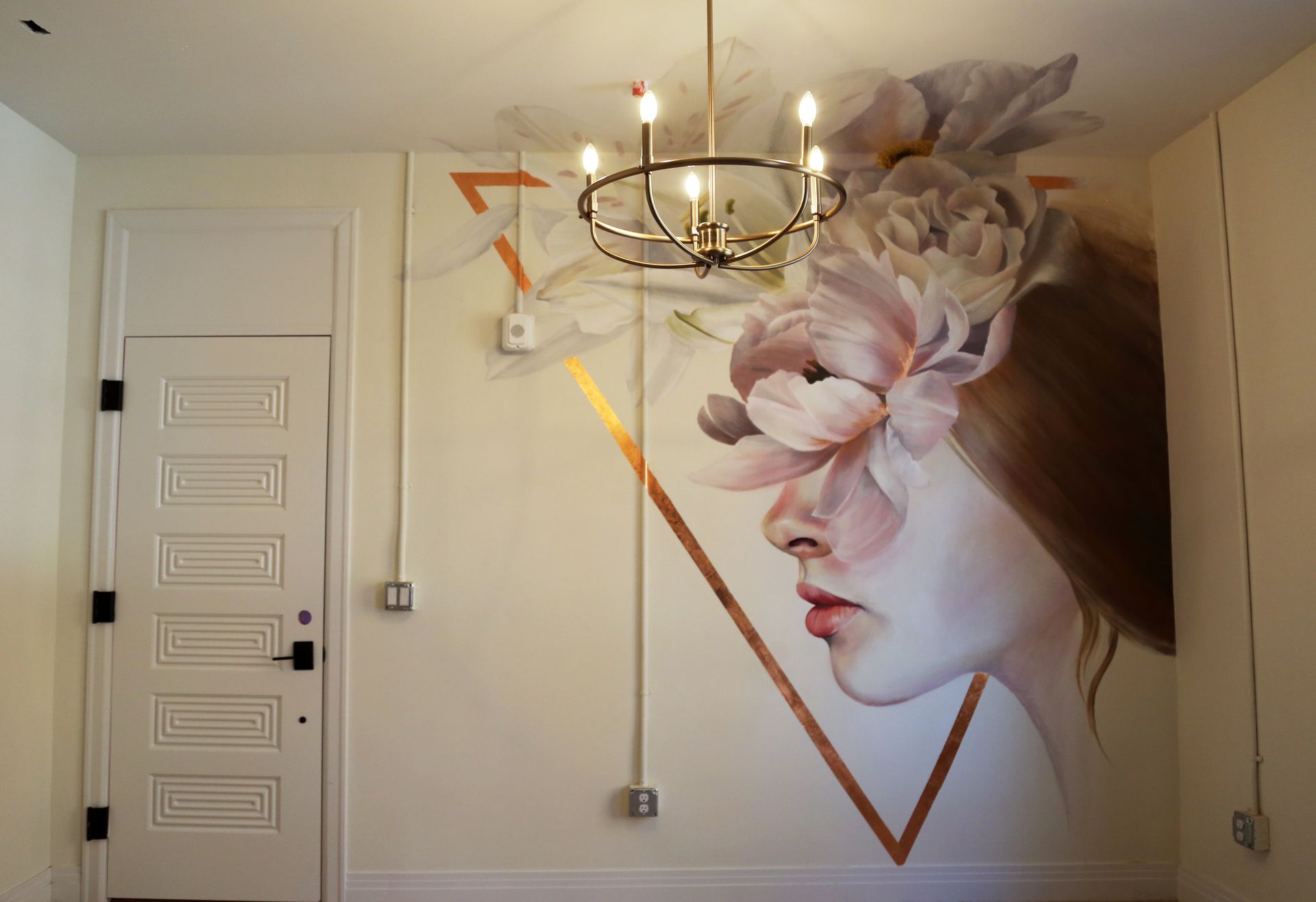 Wall mural of a woman’s profile with flowers beside a white door and chandelier in a bright room