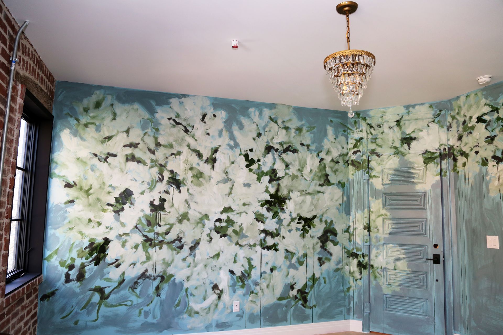 Floral mural on a blue wall in a room with a chandelier and window blinds