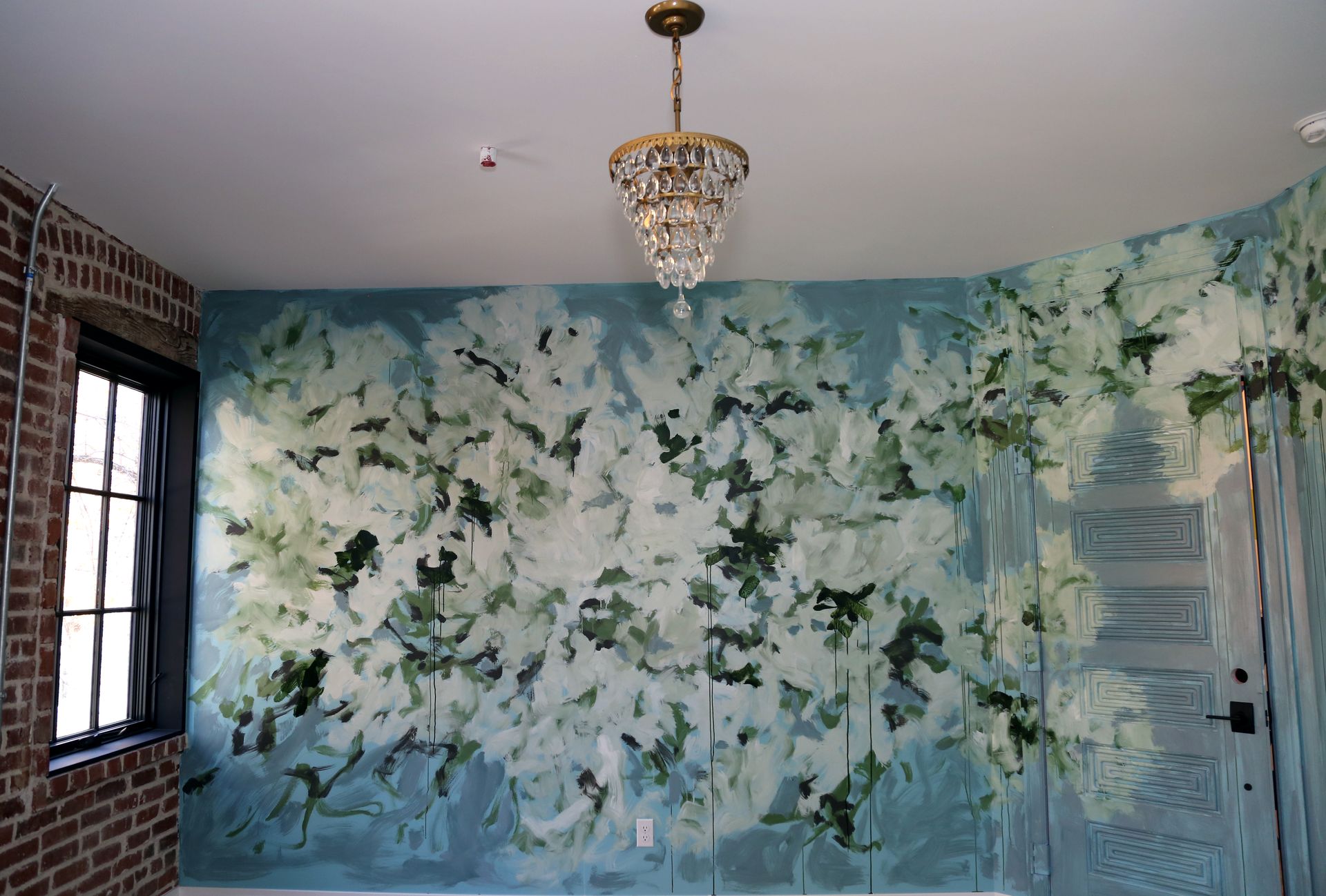 Blue floral mural in a room with a chandelier, window, and white door