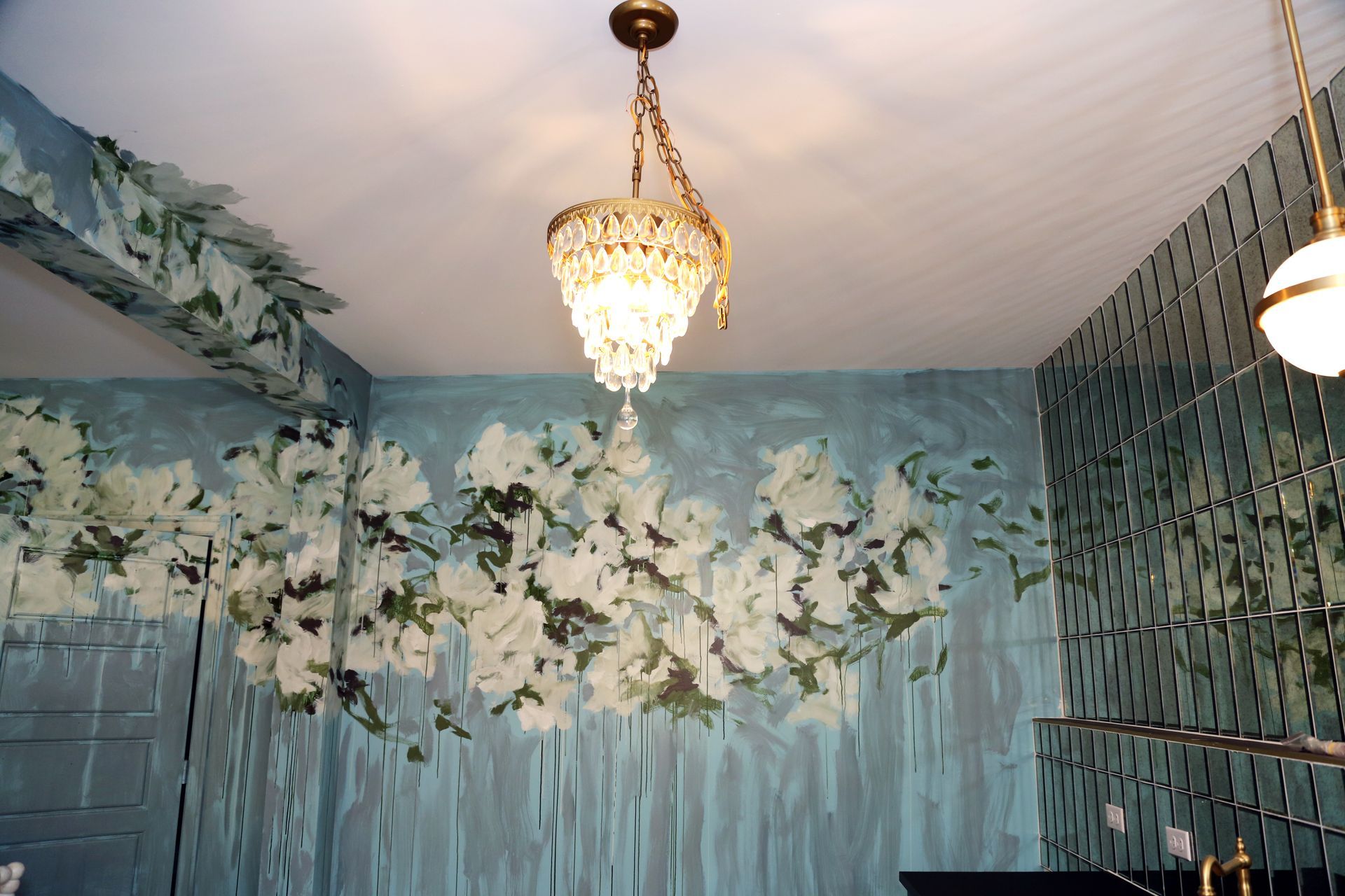 Floral mural on blue walls beneath crystal chandeliers in a decorated room