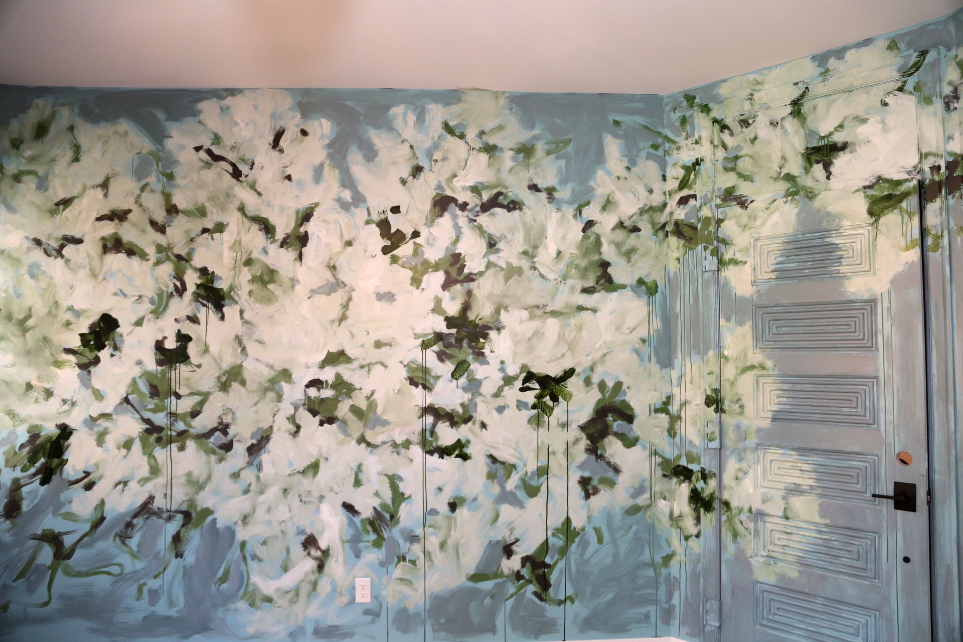 Floral wallpaper mural with white and green blossoms on a wall beside a white door
