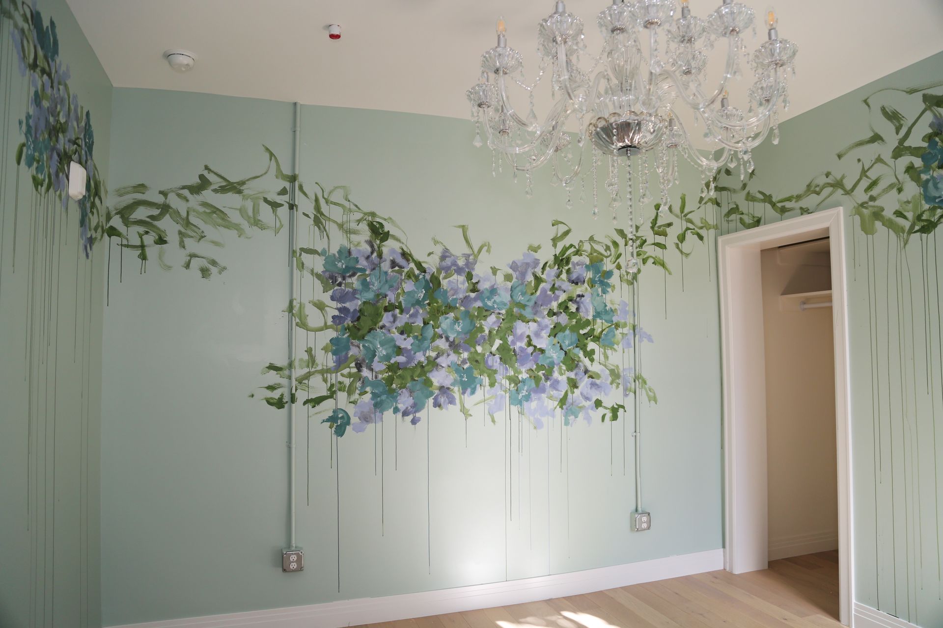 Pastel green room with floral mural and crystal chandelier above hardwood floor