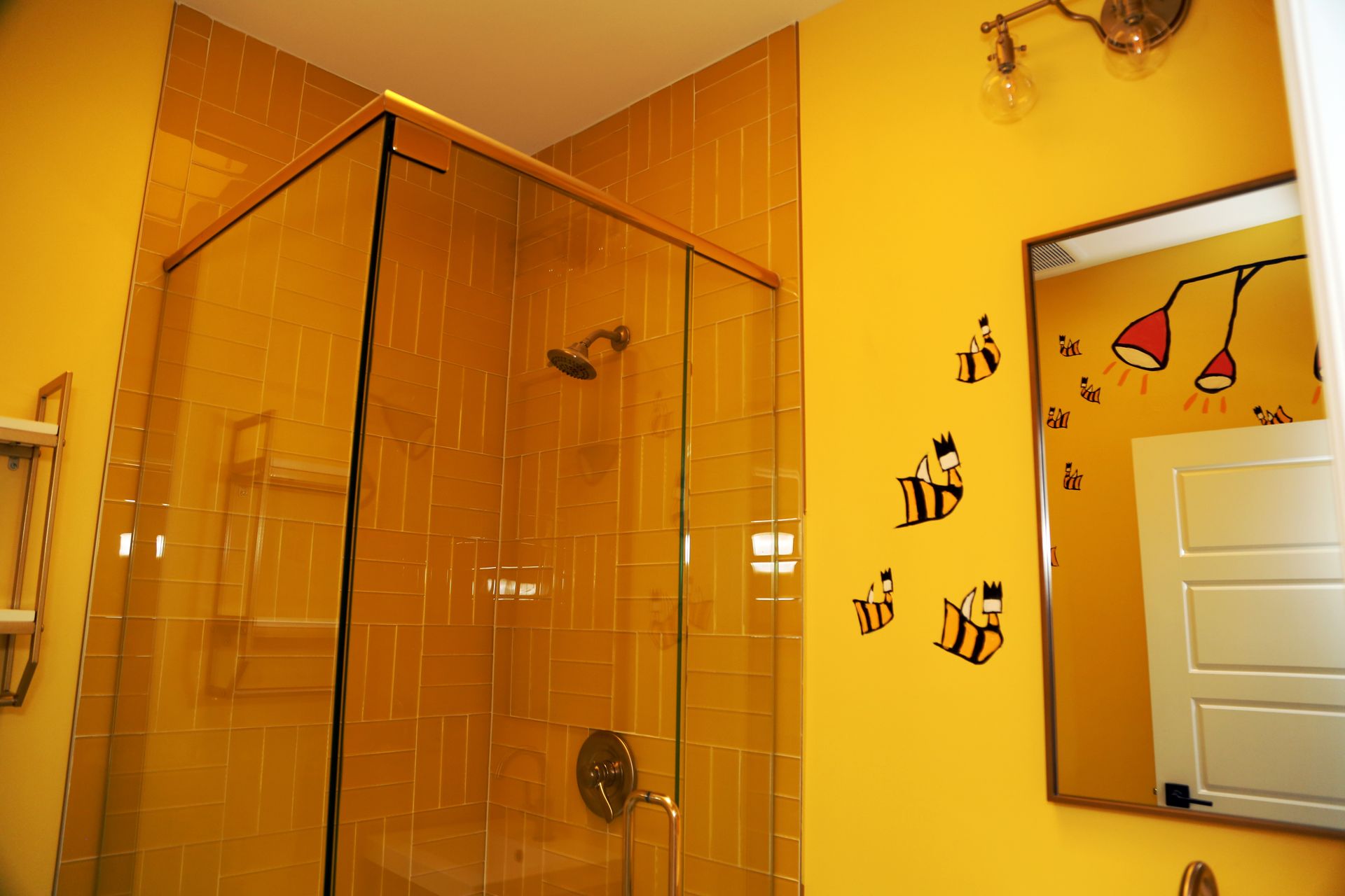 Orange-tiled bathroom with glass shower enclosure, yellow walls, and bee wall decals beside a mirror.