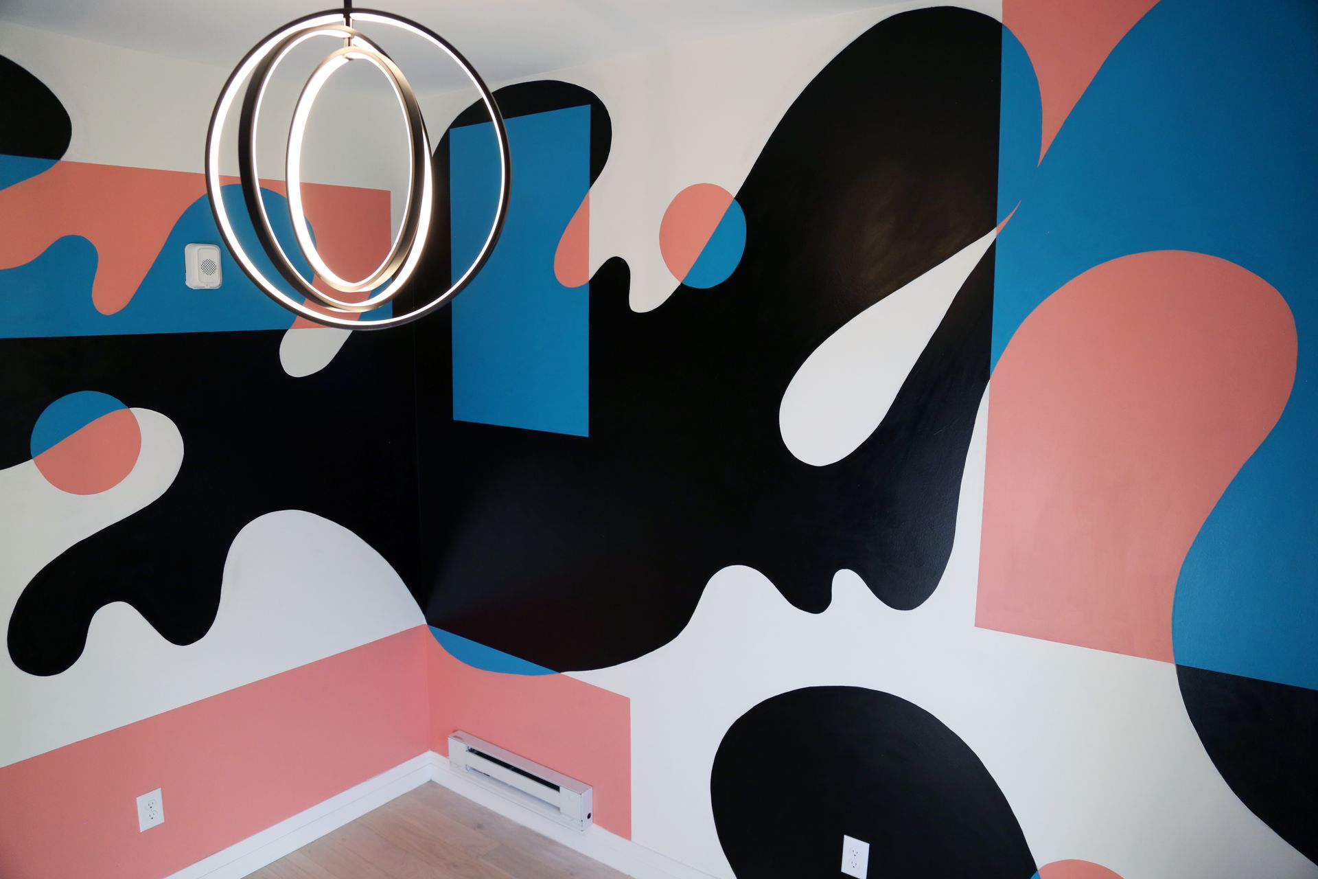 Abstract black, pink, and blue wall mural with a round mirror on a pink floorboard wall corner