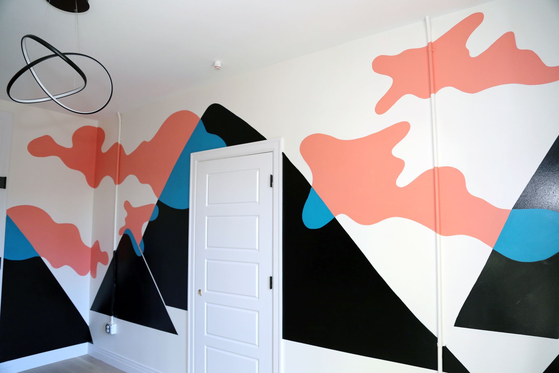 Modern room with abstract mountain mural in black, white, coral, and blue, and a white door