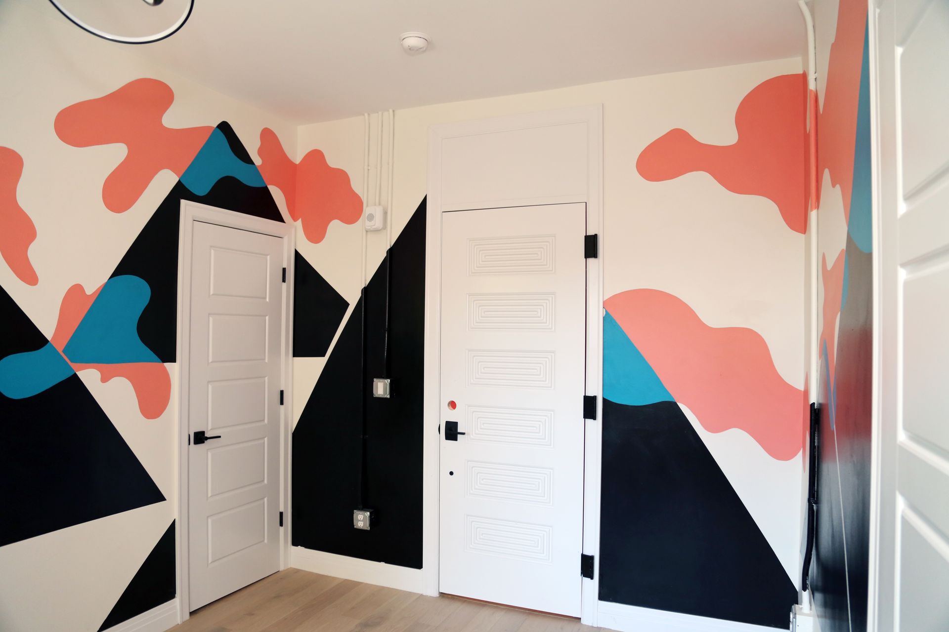 Colorful geometric mural on a hallway wall with two white doors and a black accent panel