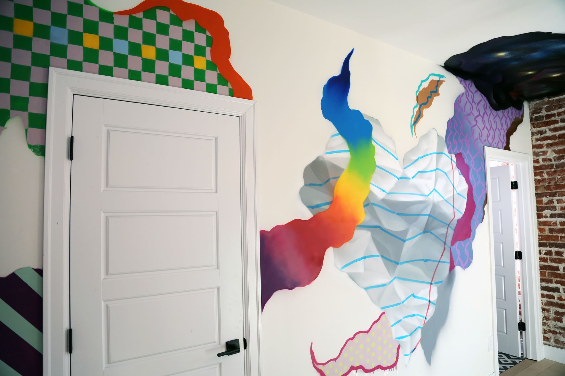 Colorful abstract mural on a white wall beside a door in a hallway