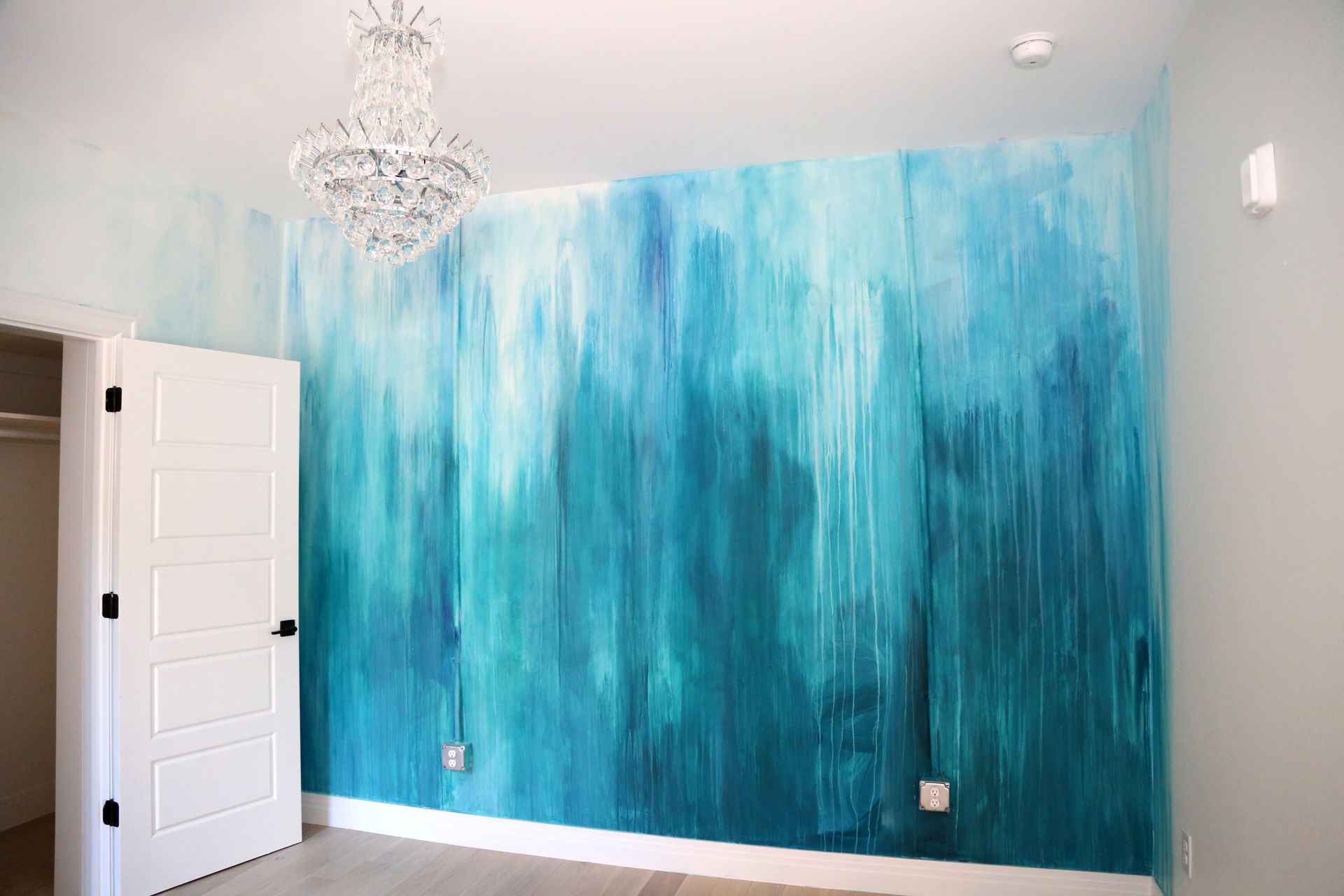 Blue textured accent wall in a bright room with a chandelier and white door.