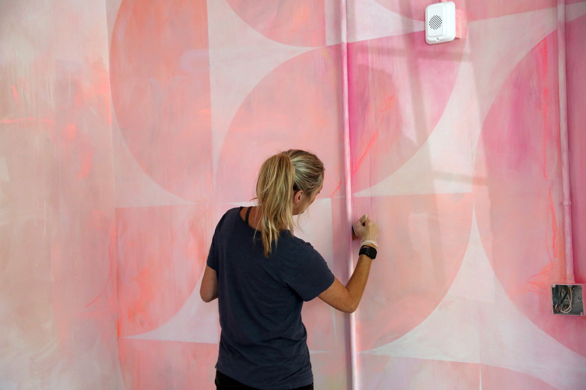 Person painting a pink wall with a roller in a room with white geometric patterns