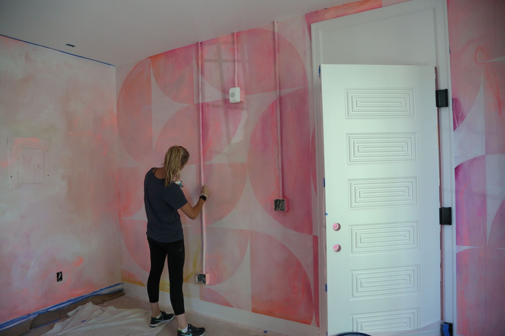 Person painting a pink wall beside a white door in an empty room