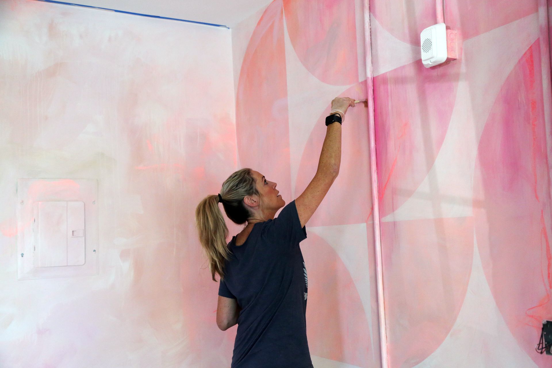 Person painting pink wall mural with a brush on a ladder