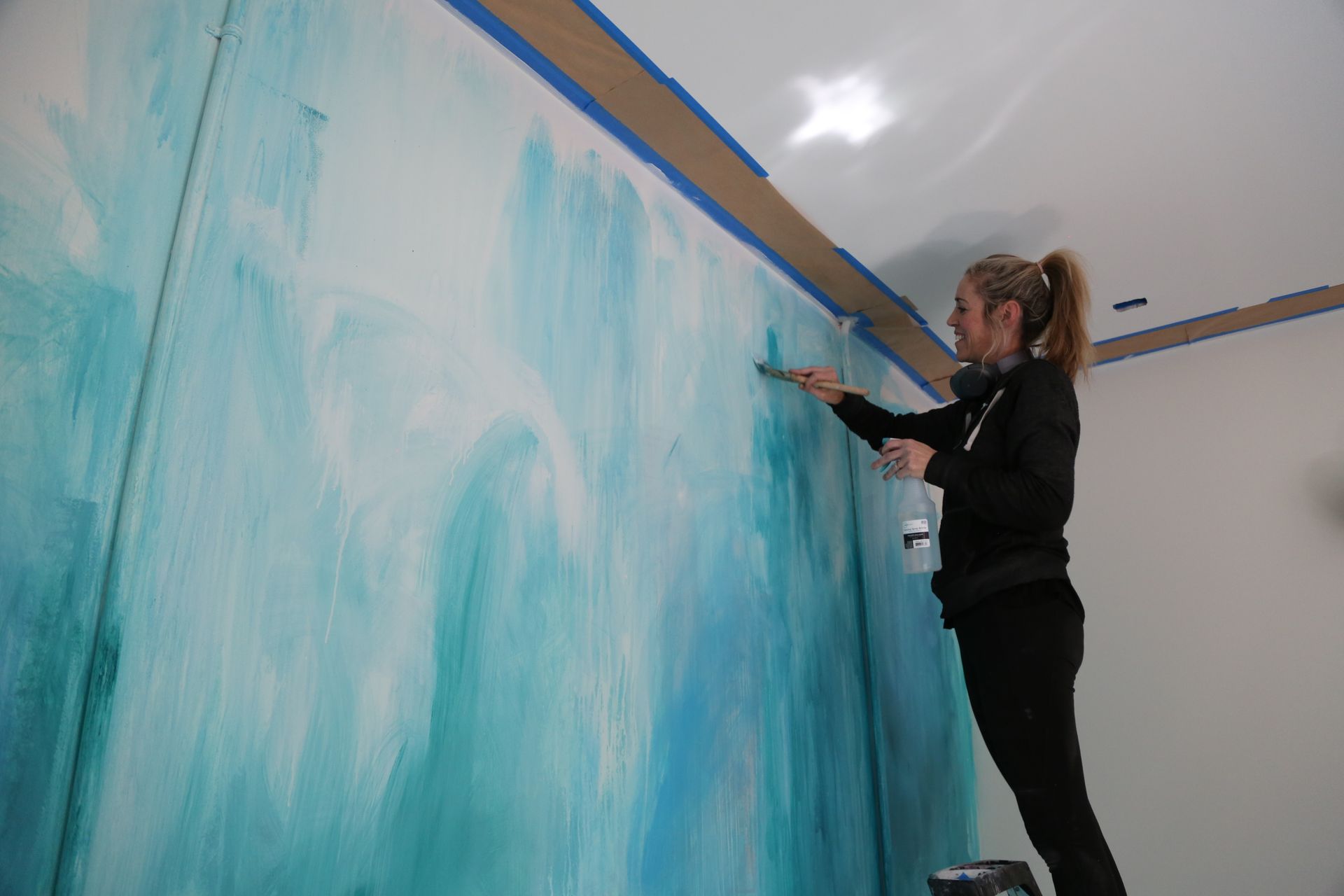Person painting a large blue wall with a paint roller indoors