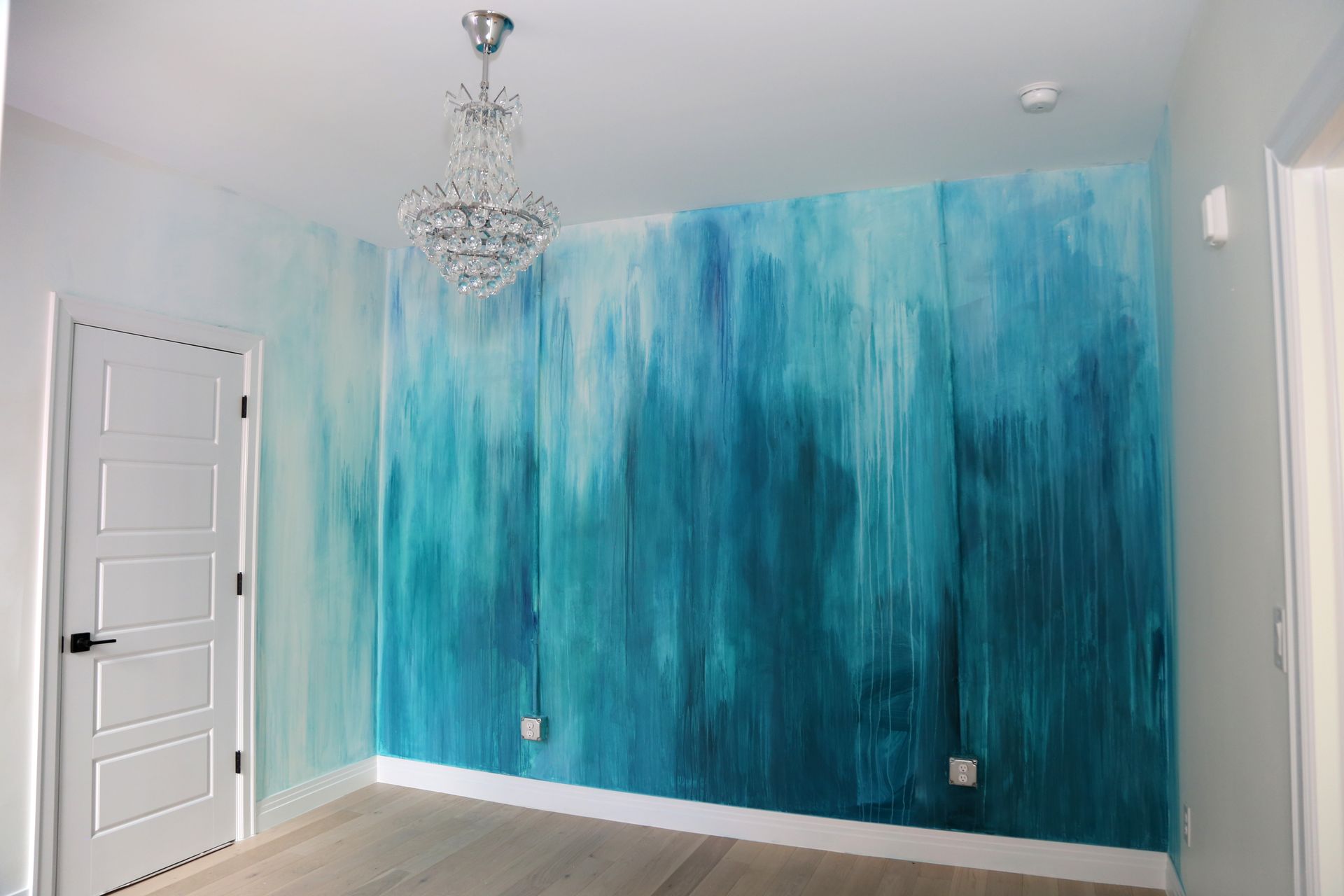 Empty room with turquoise painted accent wall, white door, chandelier, and gray flooring