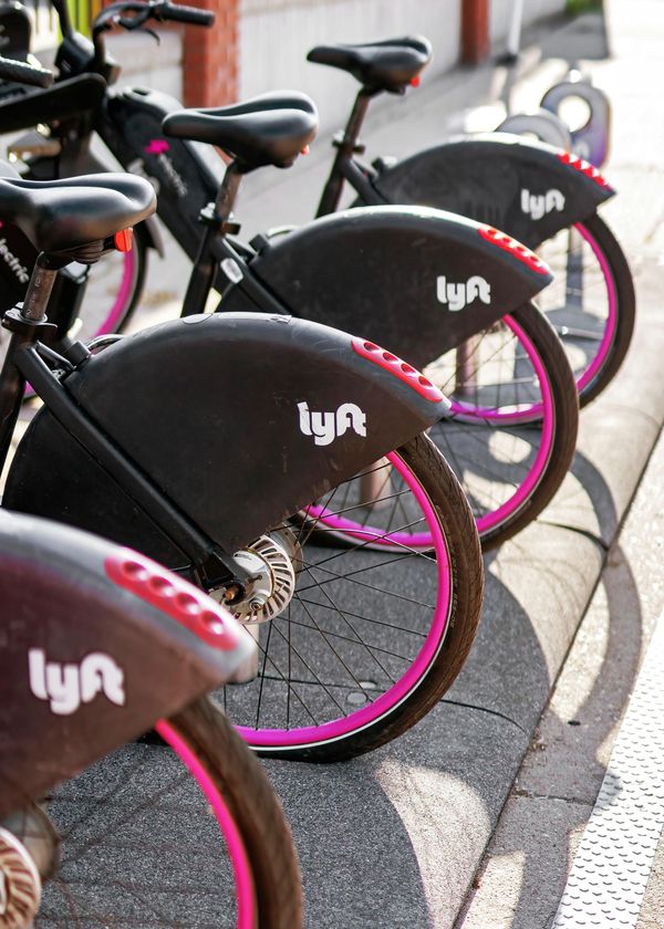 Row of Lyft bikeshare bikes with black seats and bright pink wheel rims parked along a curb