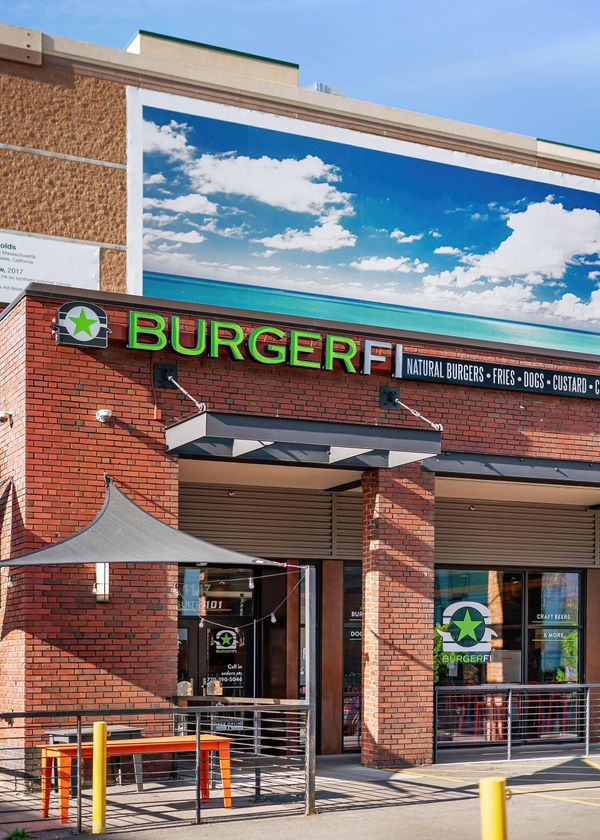 BurgerFi restaurant storefront with red brick facade and outdoor seating under blue sky