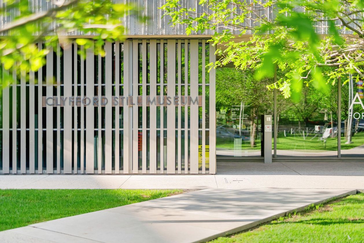Modern building entrance with vertical slats, glass doors, and green lawn and trees outside