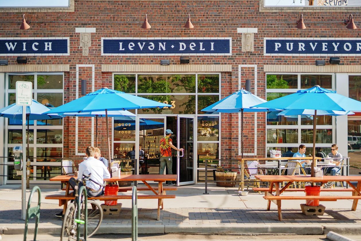 Outdoor cafe seating outside Levan Deli with blue umbrellas and a brick storefront