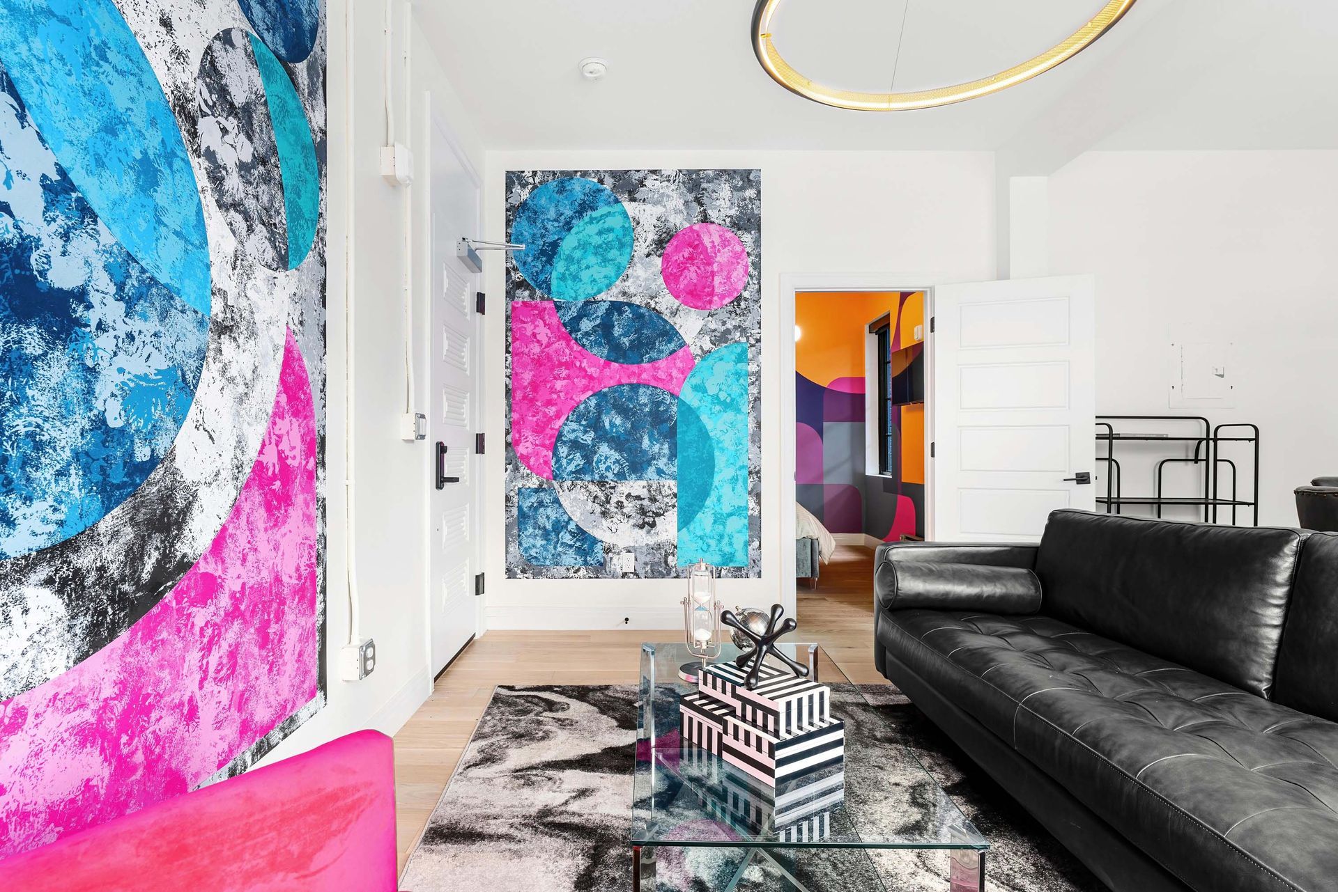 Bright modern living room with black sofa, bold pink and blue abstract art, and glass coffee table