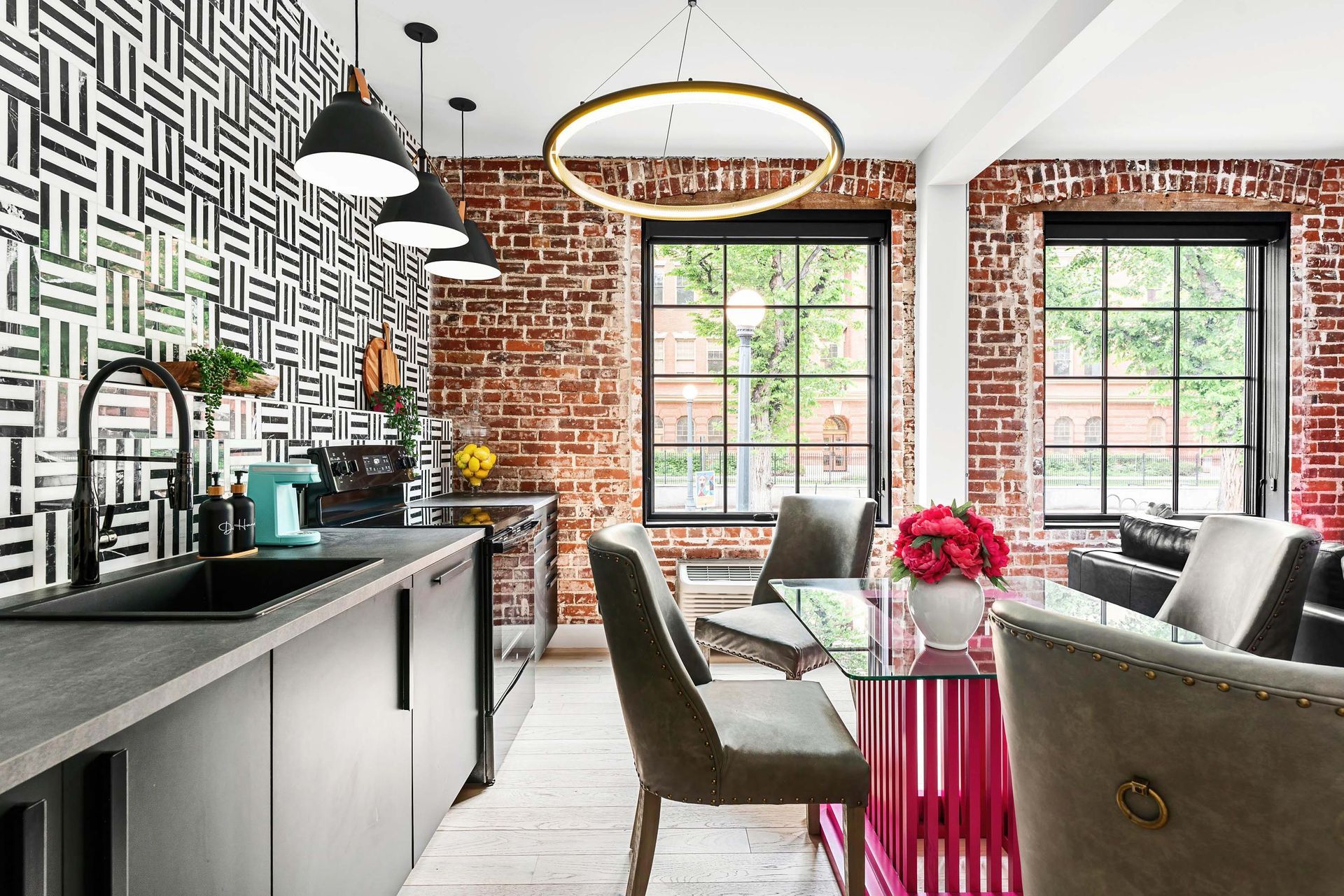 Modern loft kitchen and dining area with exposed brick, large windows, and stylish pendant lights