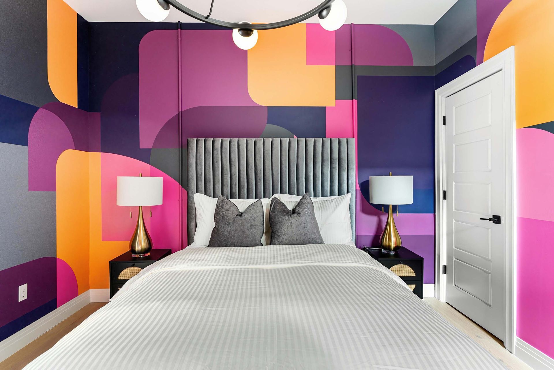 Colorful bedroom with purple geometric walls, a gray tufted bed, and white nightstands with lamps