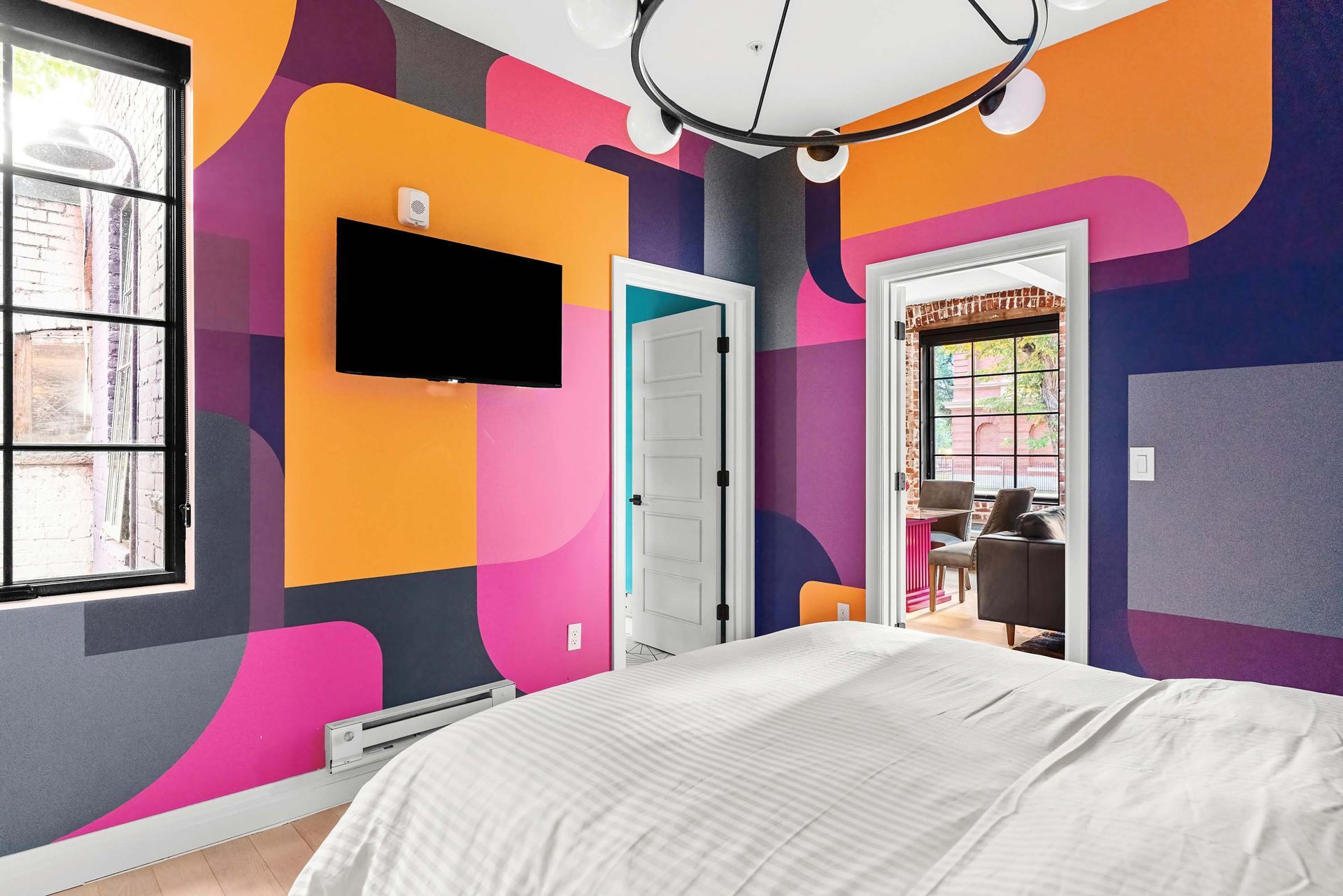 Colorful bedroom with bold pink, orange, and purple walls, a wall-mounted TV, and a white door.