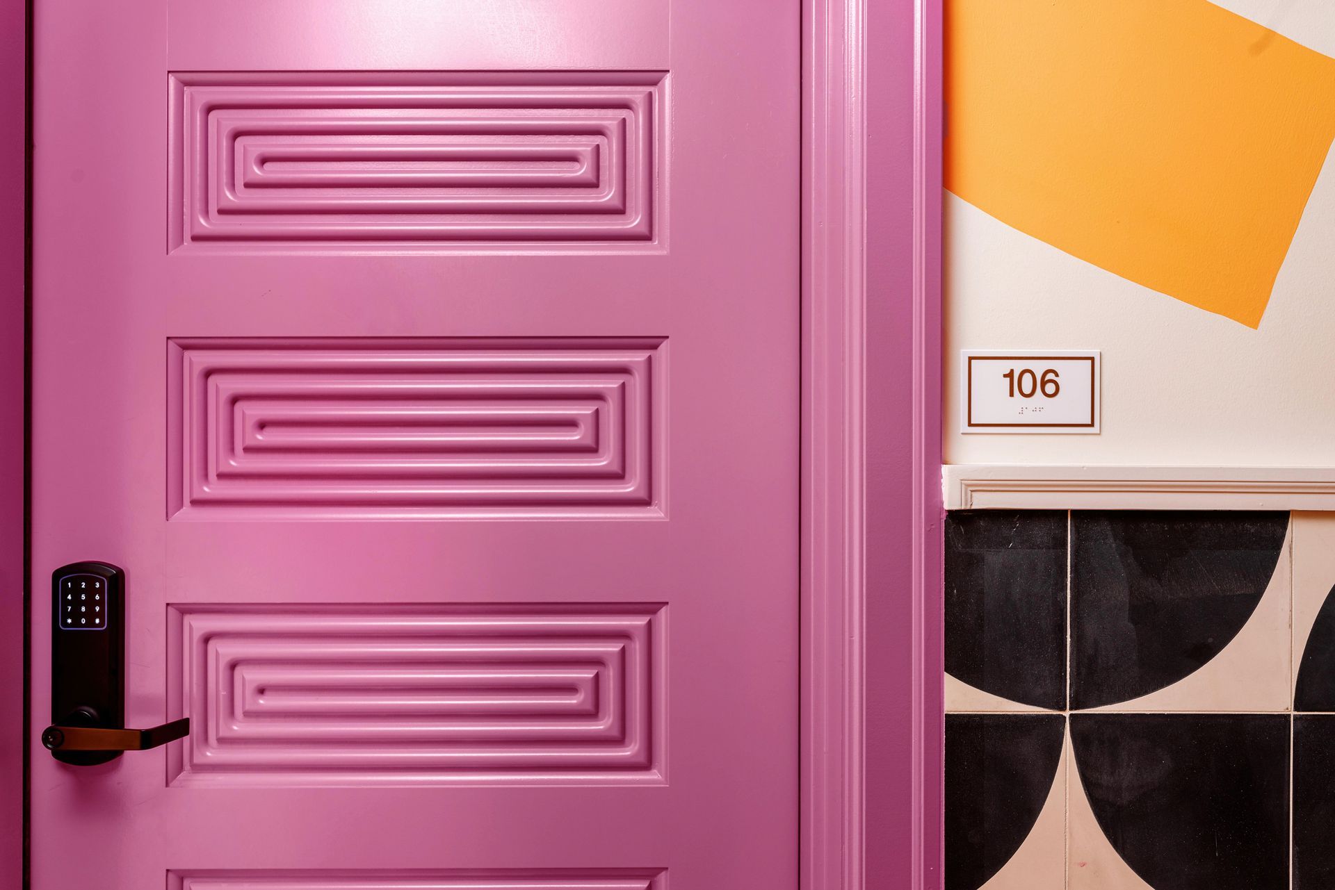 Pink door with black handle beside orange-and-white wall tile and room number 106