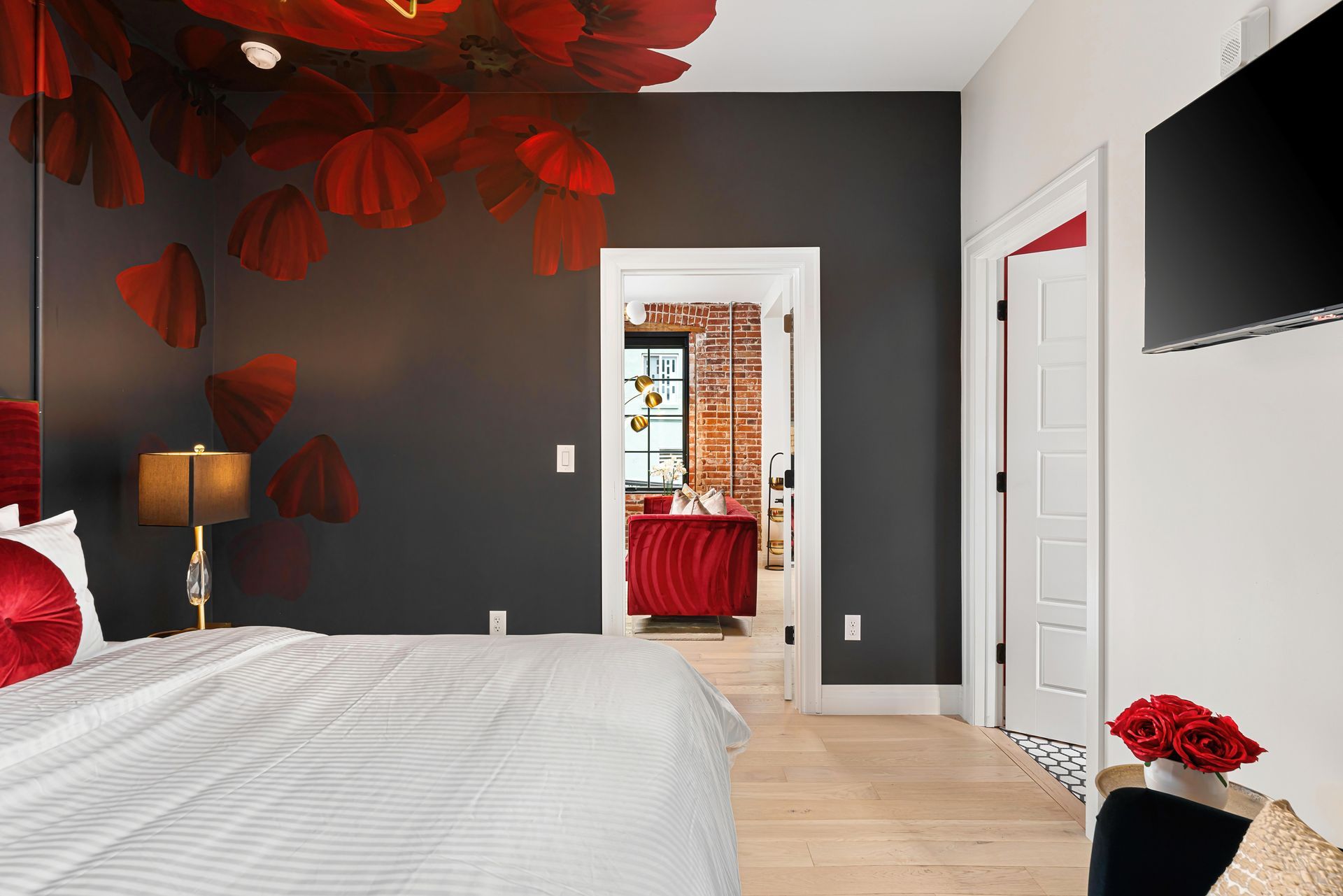 Red and black bedroom with bed, lamp, white doors, and wall-mounted TV.