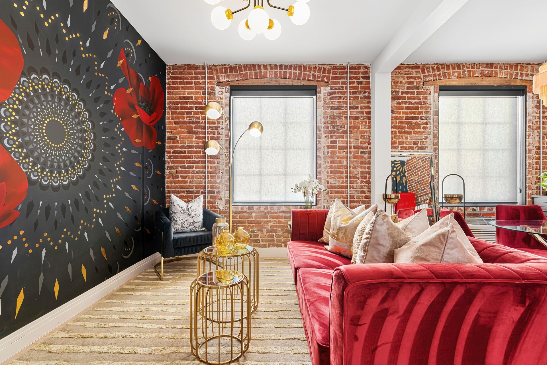 Bright loft living room with red sofa, brick walls, patterned accent wall, and gold decor