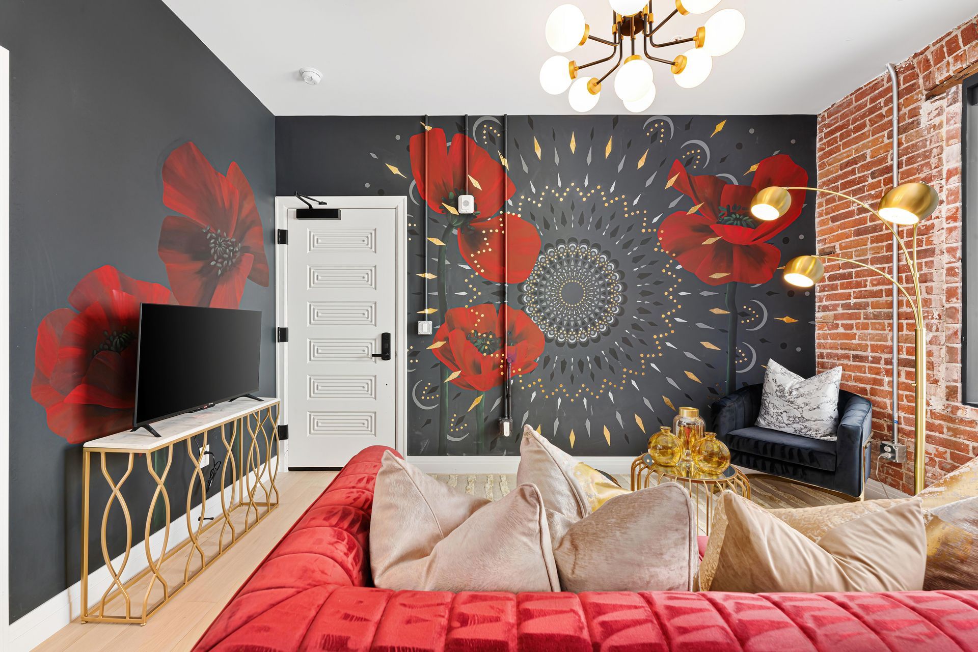 Modern bedroom with red accents, floral mural wall, brick feature wall, and TV on a gold console