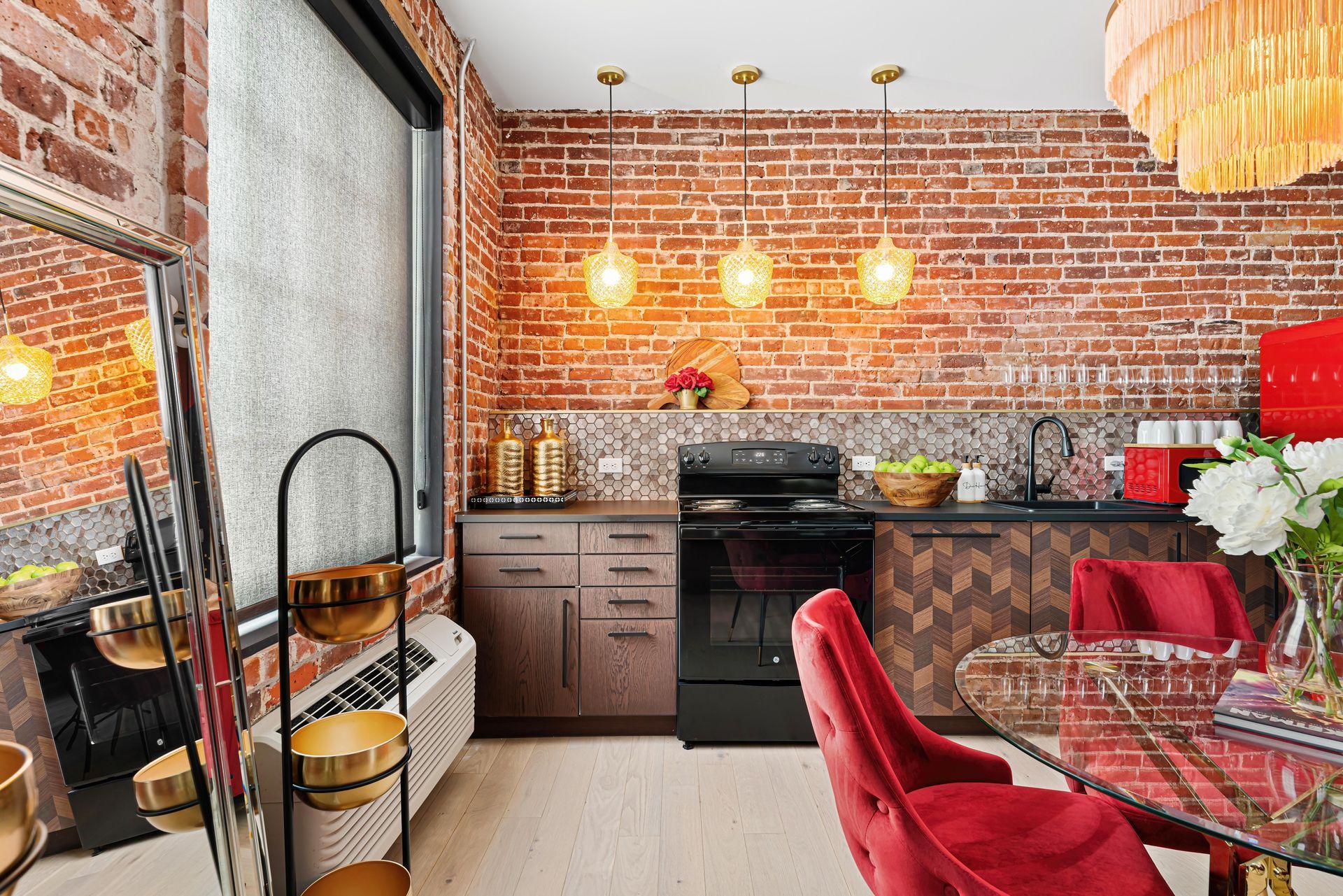 Modern kitchen and dining area with brick walls, red chairs, and hanging pendant lights