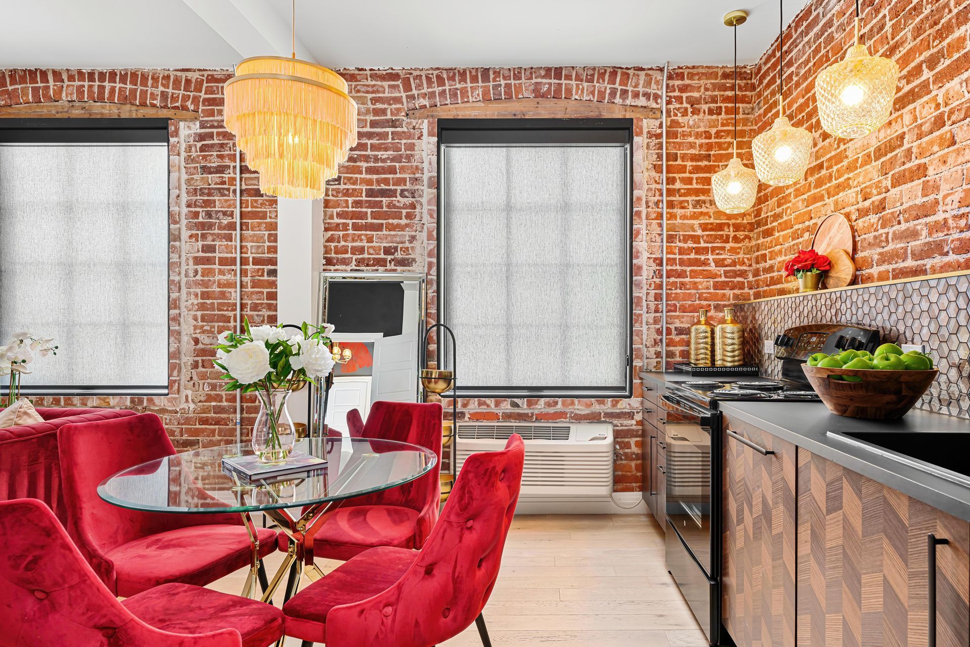 Bright dining nook with red chairs, round glass table, exposed brick walls, and large windows