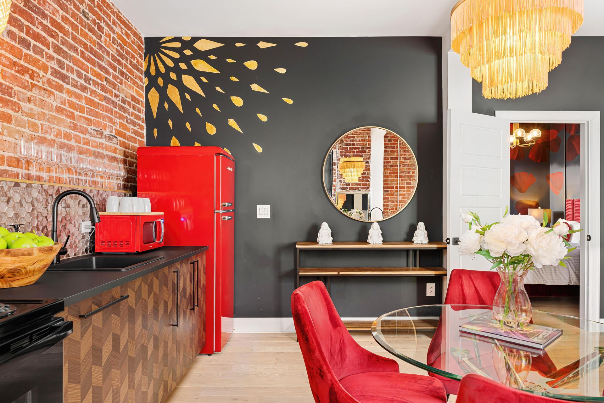 Stylish dining area with red chairs, black walls, exposed brick, and a red refrigerator