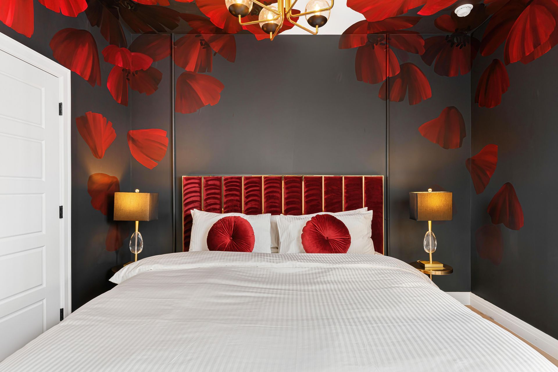 Romantic bedroom with red heart decorations, dark walls, white bed, and warm bedside lamps