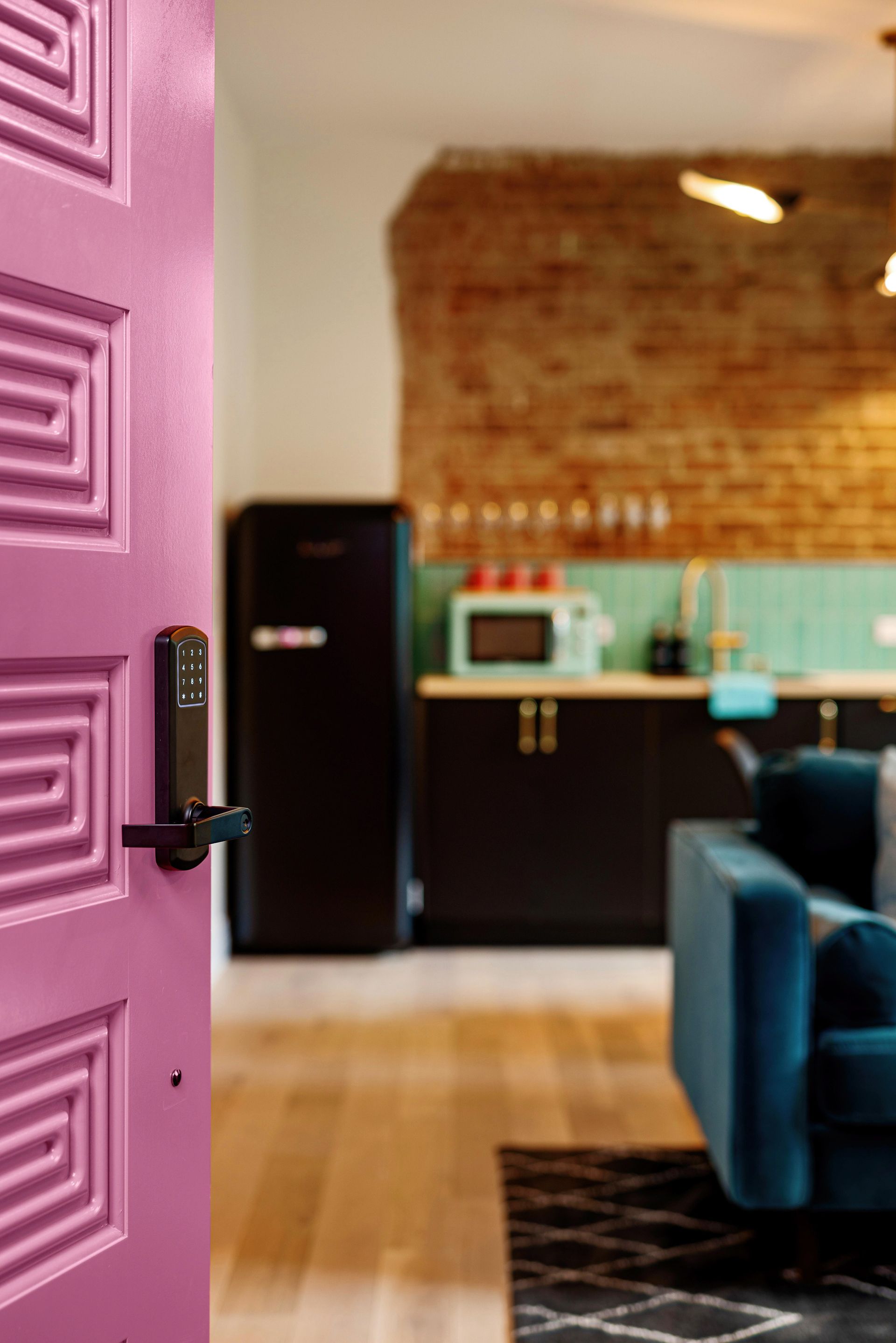 Open purple door leading to a modern living room with brick wall, teal backsplash, and blue sofa