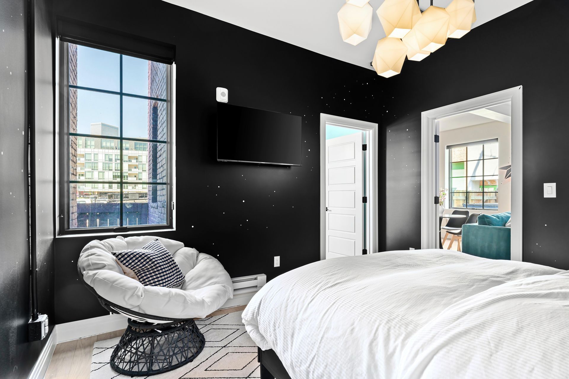 Modern bedroom with black walls, white bedding, a window, TV, and a hanging chair